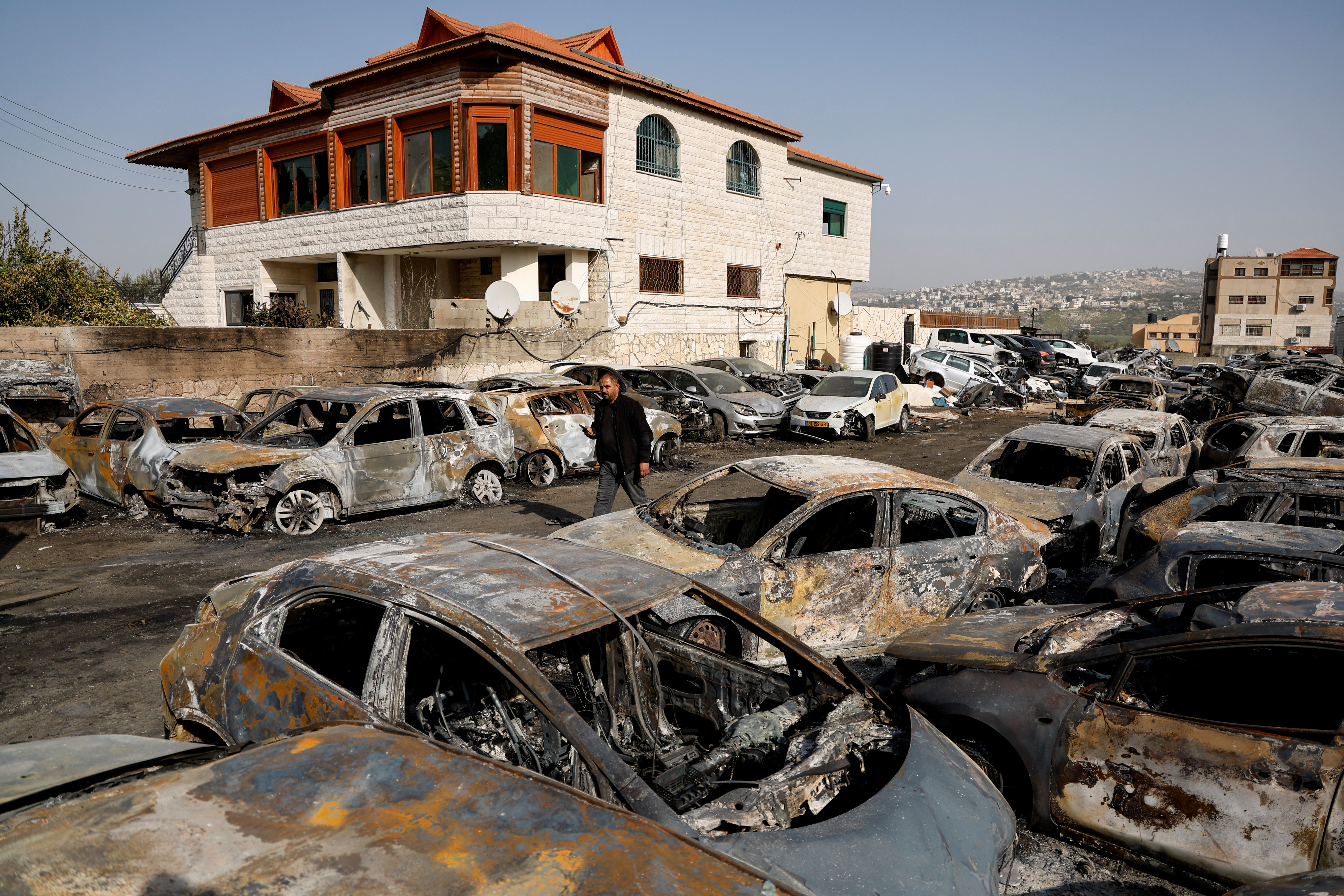A man walks among cars burned in an attack by Israeli settlers after a Palestinian gunman killed two Israeli settlers near Huwara in the Israeli-occupied West Bank on February 27, 2023