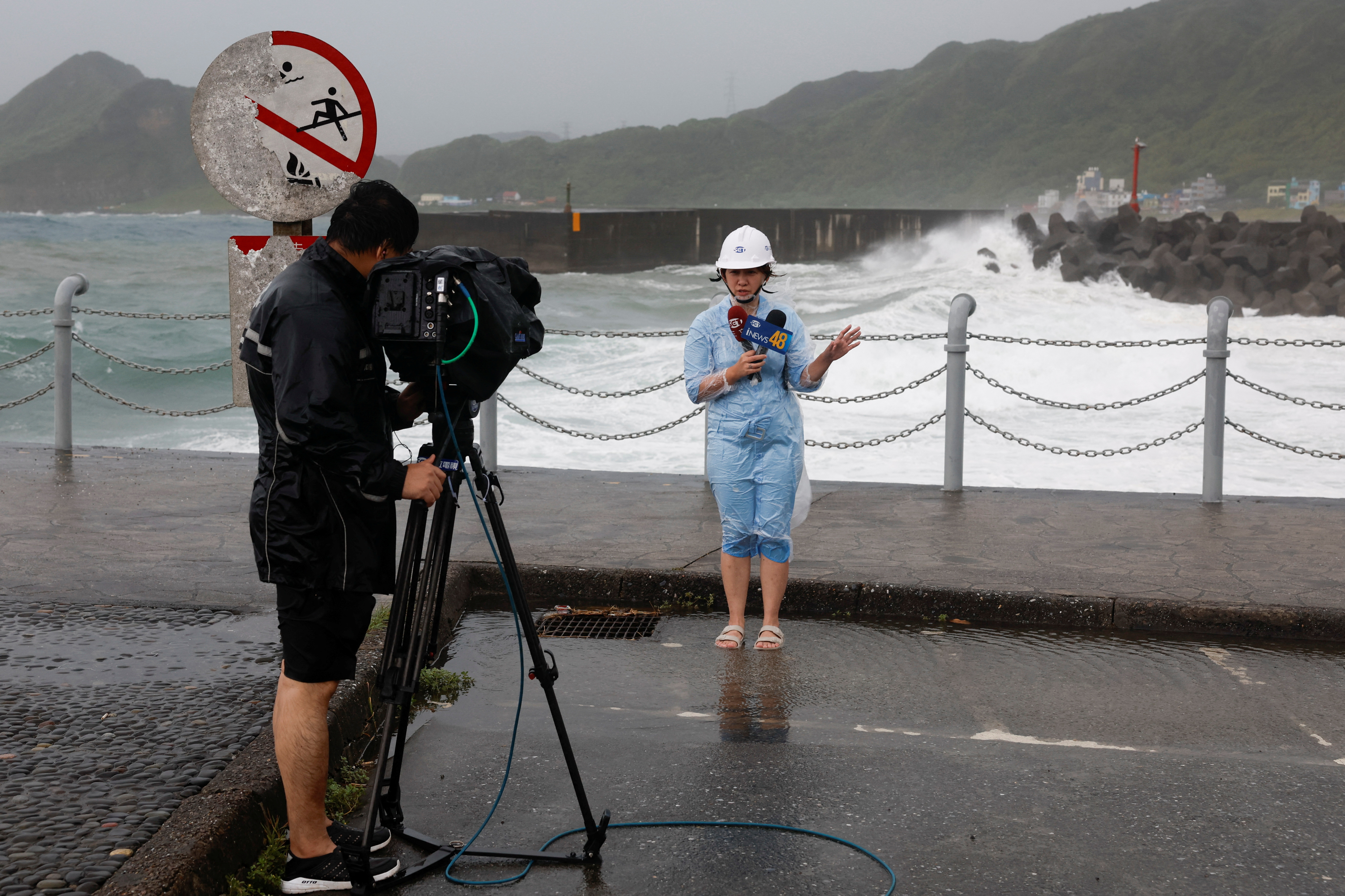 Media members report near the shore while waves break against the shore protections as Typhoon Gaemi approaches in Keelung, Taiwan July 24, 2024. REUTERS/Carlos Garcia Rawlins