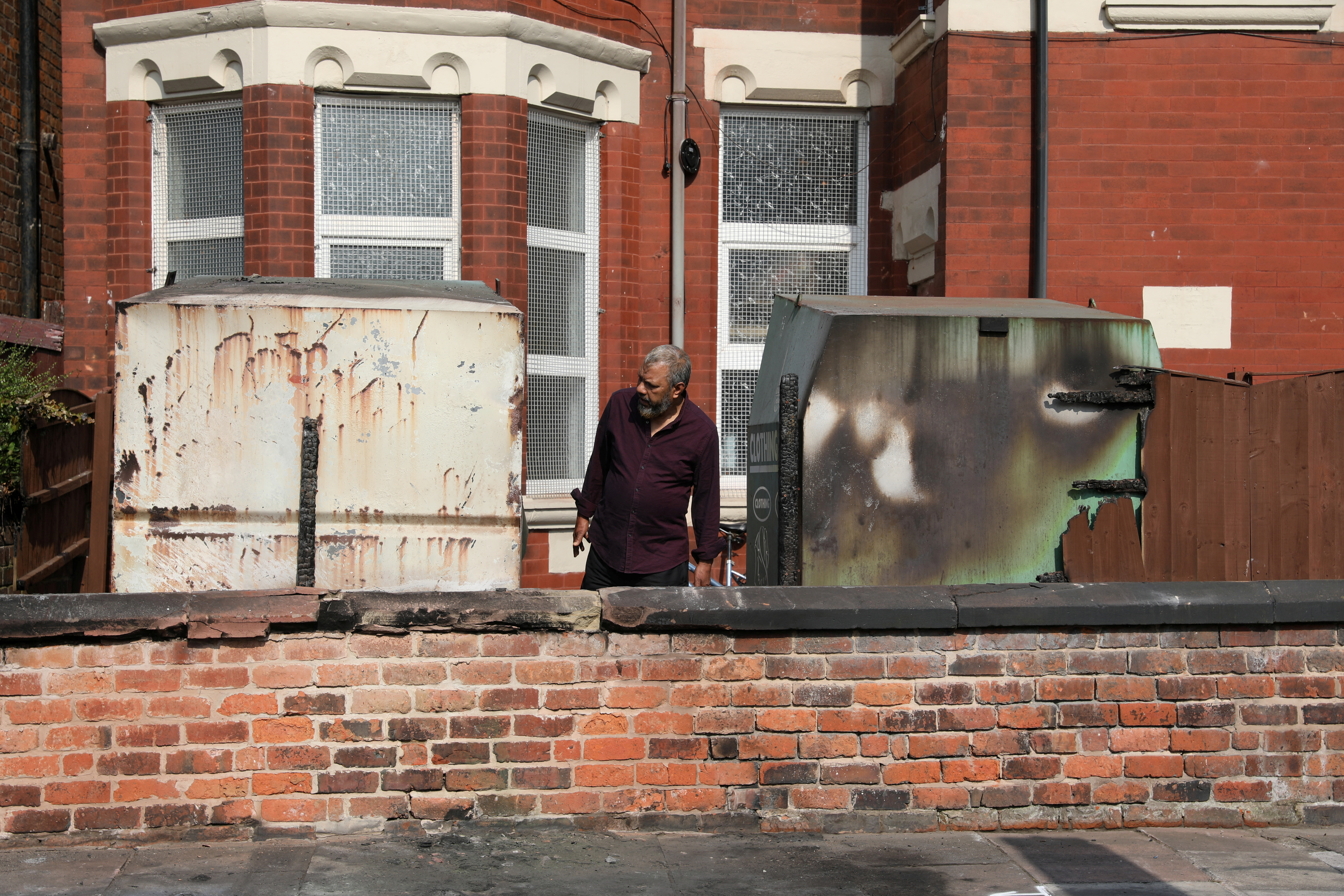 A man inspects damaged clothing bins and a fence of the Southport Islamic Society Mosque,