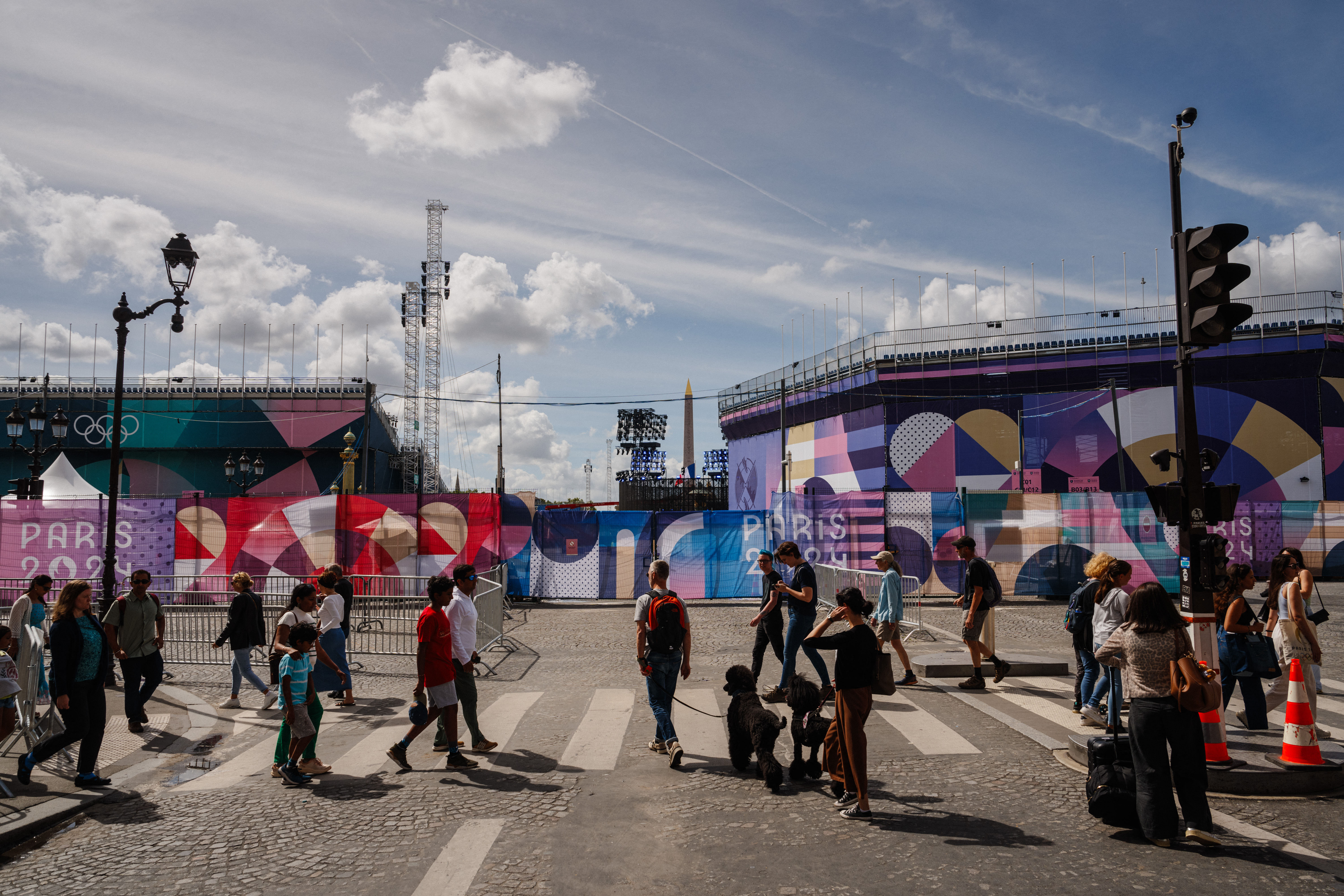 Pedestrians walk by the Place de la Concorde Paralympic site covered in "Paris 2024" tarpaulins in Paris, on August 21, 2024, ahead of the Paris 2024 Paralympic Games. - The Place de la Concorde will be hosting the Paris 2024 Paralympic Games opening ceremony on August 28, 2024. (Photo by Dimitar DILKOFF / AFP)