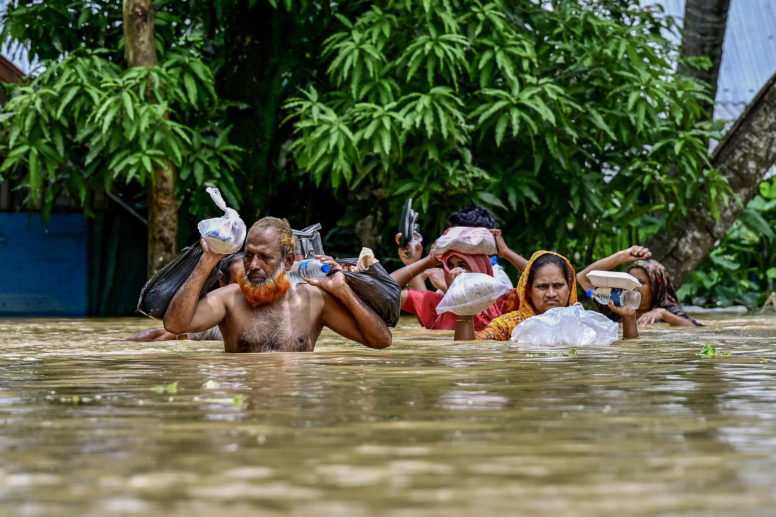 People carrying relief materials wade through flood waters in Feni
