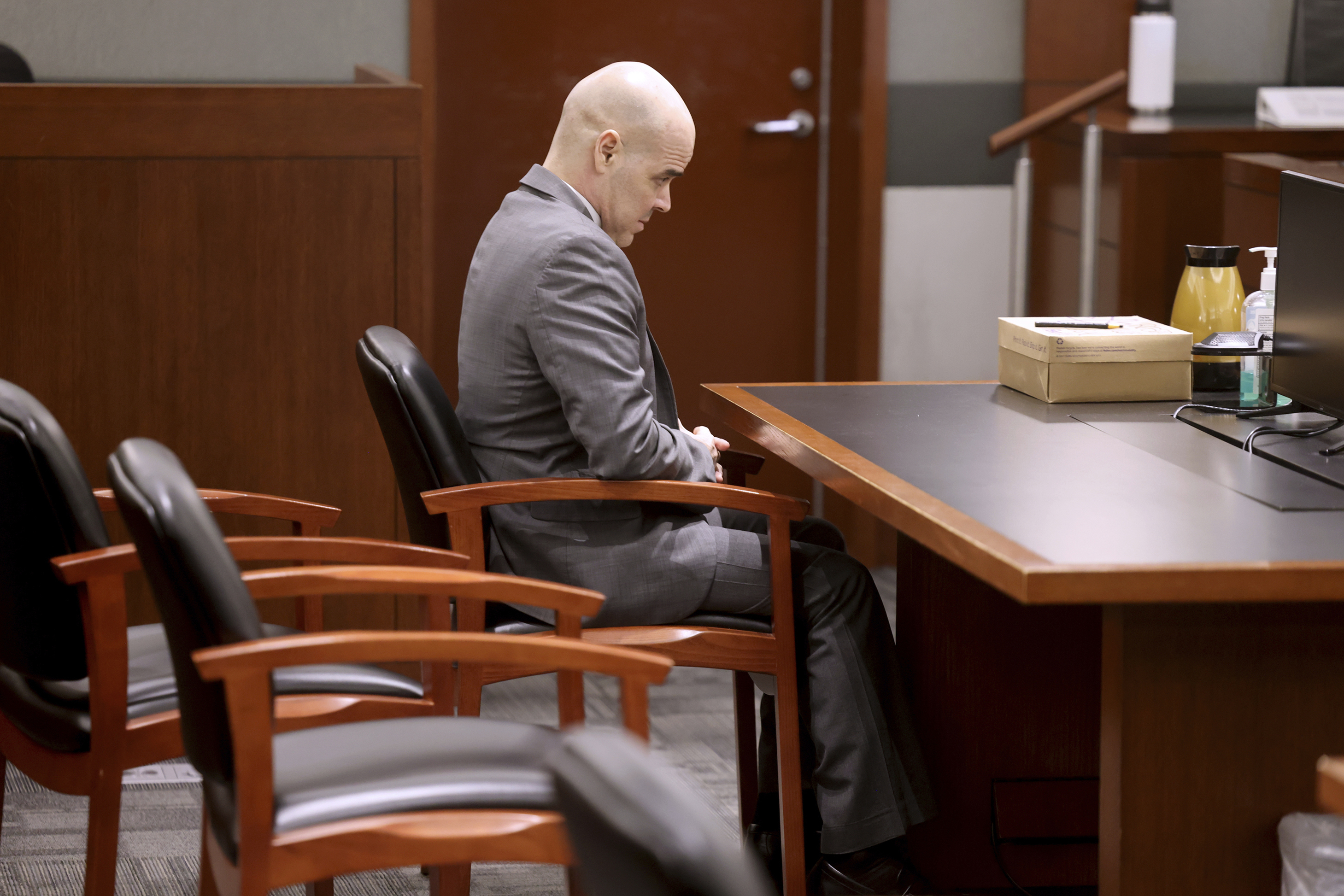 Robert Telles in court, He is bald. He is wearing a light grey suit and sitting at a chair. He has hands in his lap and his head bowed.
