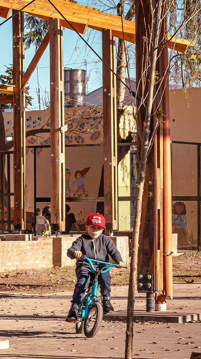 Kids ride bicycles beneath the scaffolding of the future La Corcova library