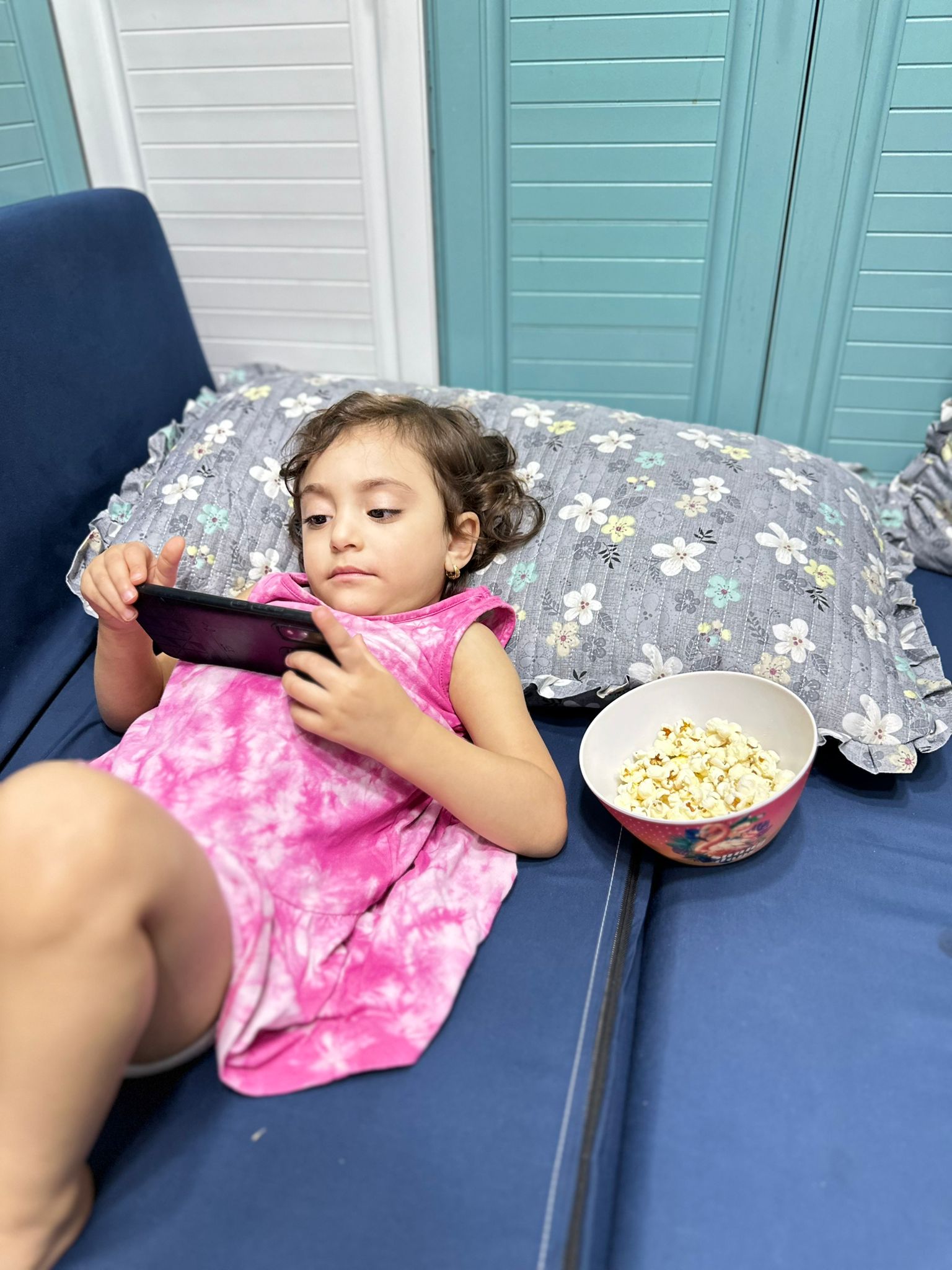 Saja’s niece Alaa watches videos on a mobile phone while lying on the mattress in the kitchen [Coutesy of Saja Bawaqneh]