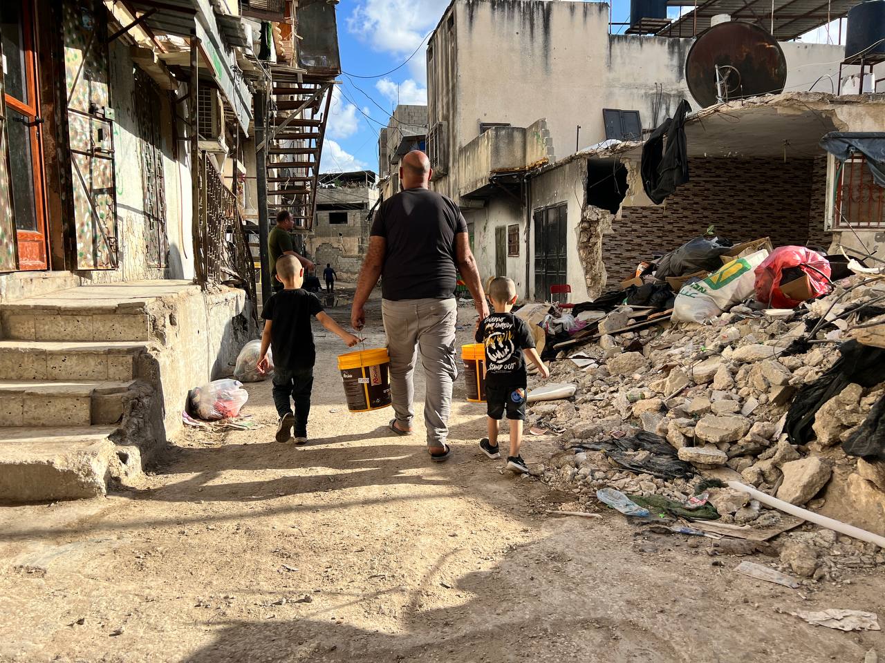 Akram Nassar and his children carry water to their home from a nearby water tank, in Tulkarem refugee camp, occupied West Bank, September 16, 2024 [Al Jazeera]