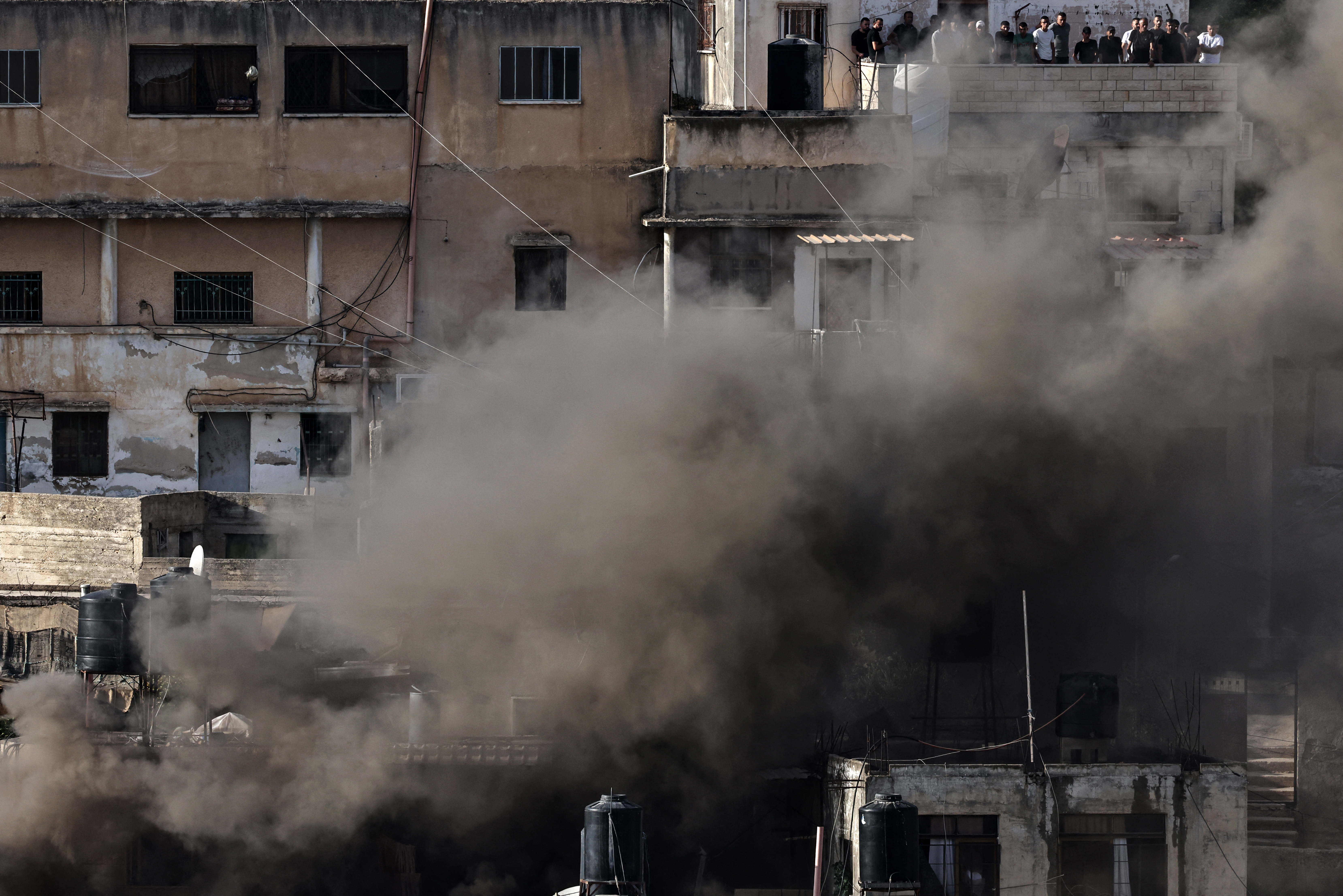 People peek out of a balcony as smoke billows in the Jenin refugee camp on September 19, 2024