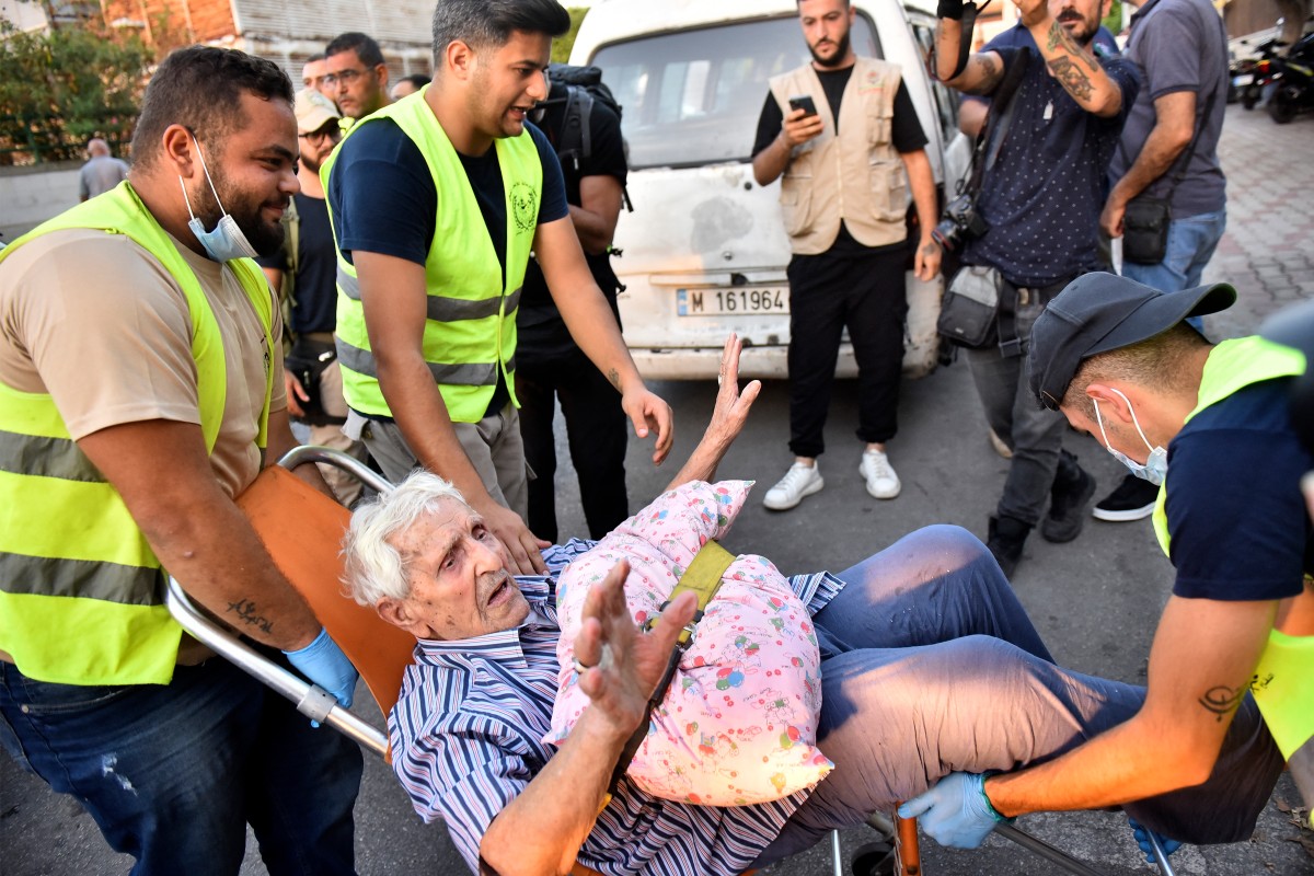 Volunteers carry an elderly displaced man on a chair displaced Lebanese people are received at an art institute transformed into a shelter in Beirut, on September 23, 2024