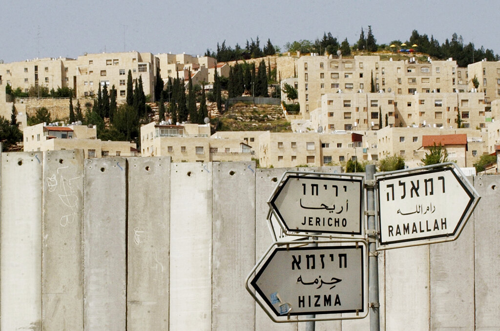 The Jewish settlement of Pisgat Ze’ev is visible behind a section of Israel’s separation barrier, as road signs point to the Palestinian towns of Jericho, Ramallah, and Hizma, in the occupied West Bank village of Hizma, near Jerusalem, in 2005. Israel took inspiration from apartheid South Africa’s racial segregation policies