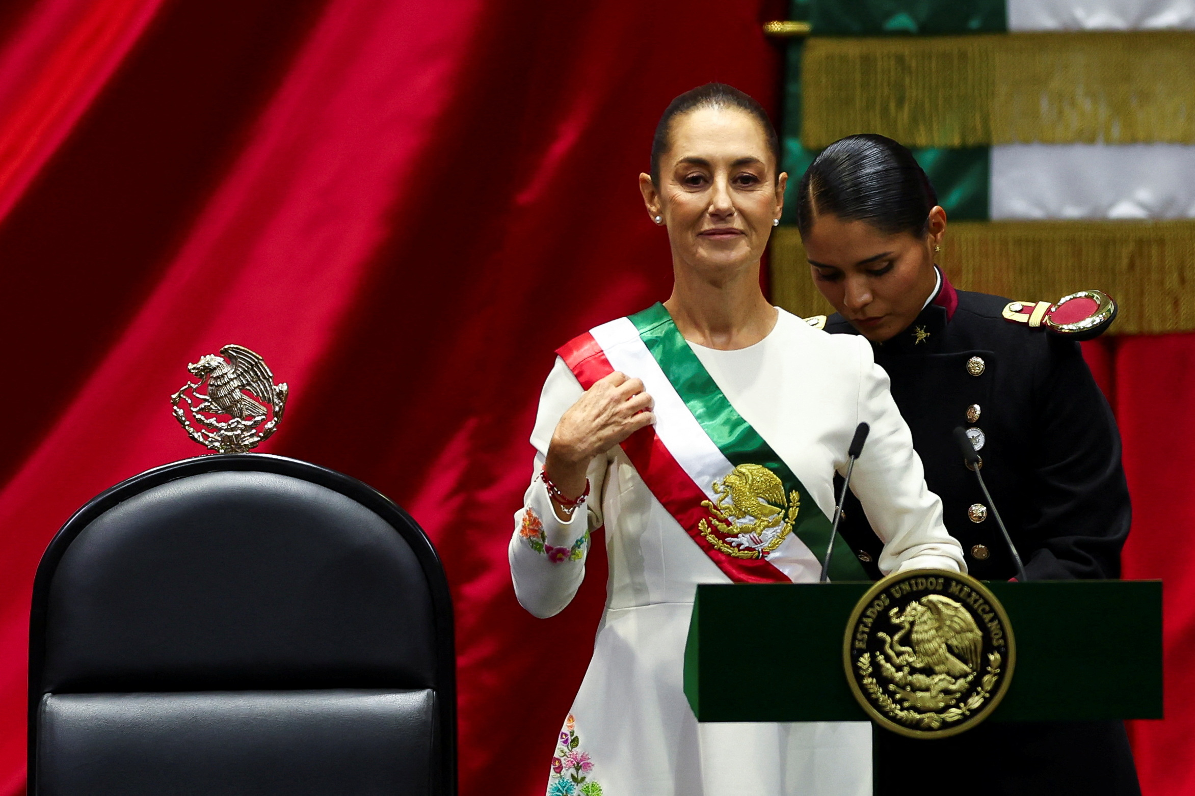 Mexico's new President Claudia Sheinbaum is assisted while putting on the sash during her swearing-in ceremony at Congress, in Mexico City, Mexico, October 1, 2024 [Raquel Cunha/Reuters]