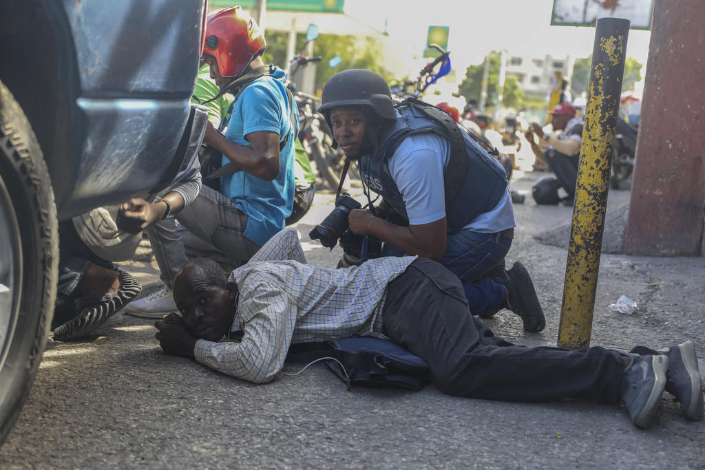 People take cover behind a car during a gun battle