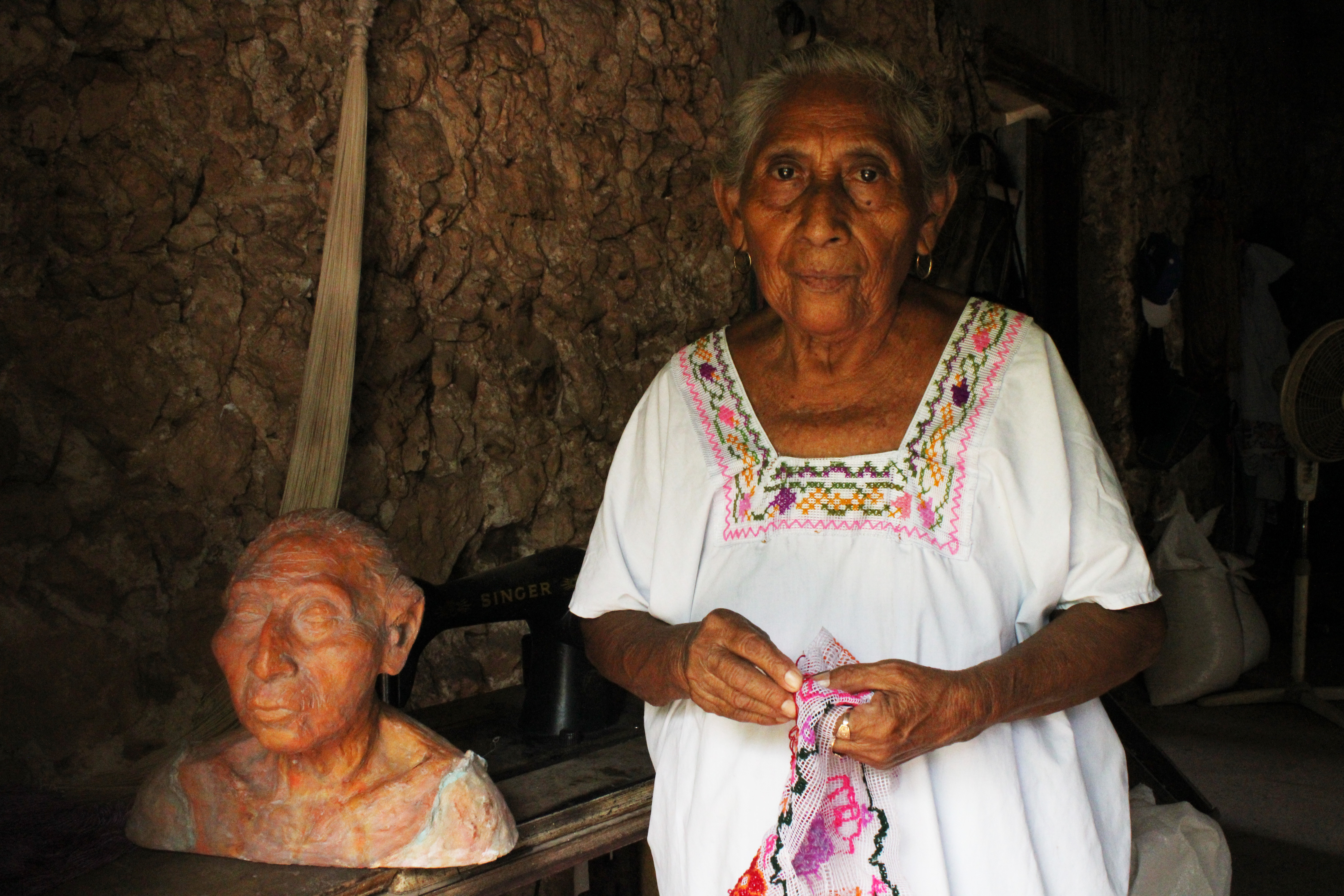 Catalina Kankub Hab, 85, a seamstress from Dzan, Yucatán, Mexico, stands next to her self-sculpture made by Luis May Ku, 49, and adorned with Maya Blue paint inside her home on 9 September, 2024