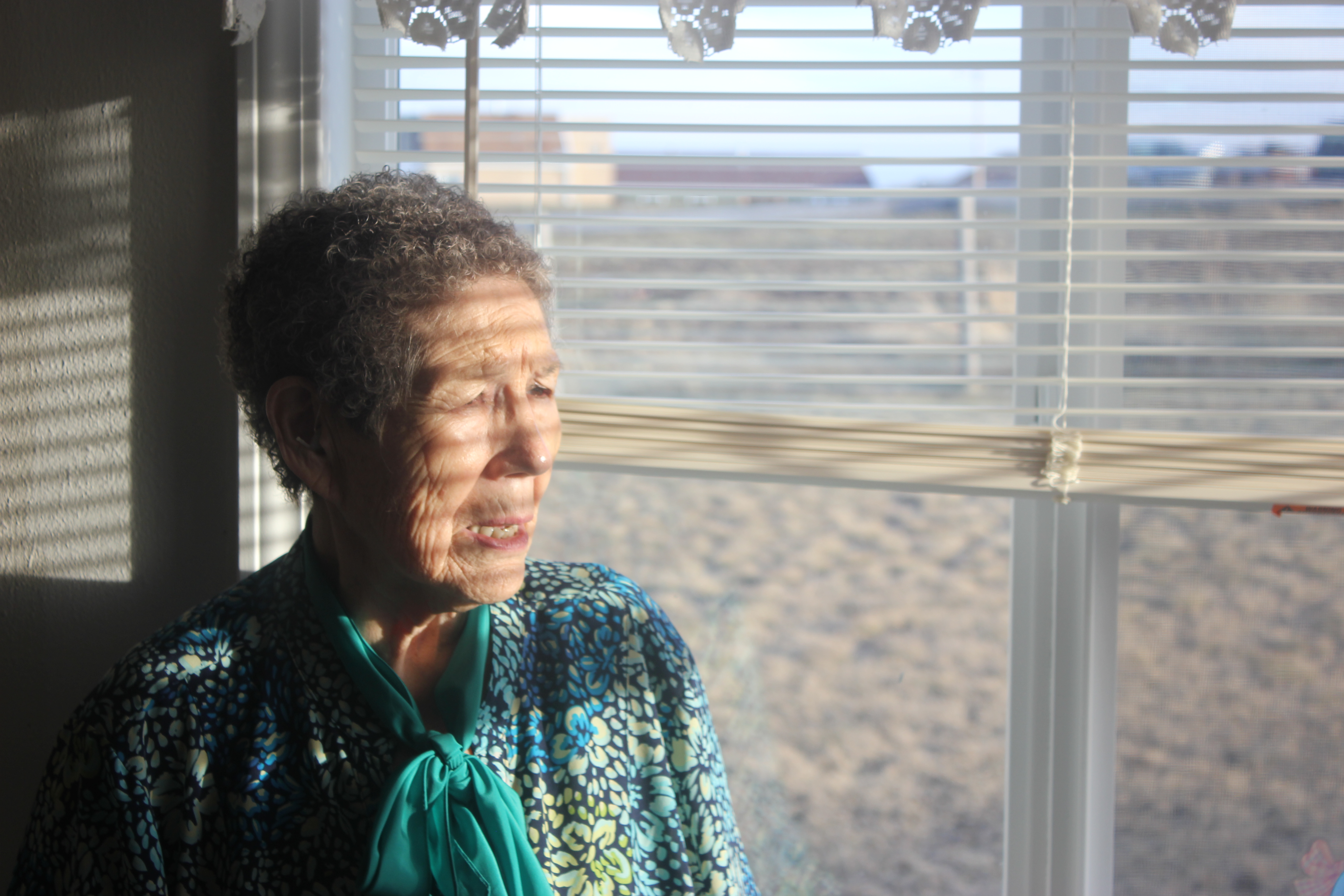 Angeline Mad Plume-Aimsback, Rosalyn LaPier’s mother and an Indigenous boarding school survivor, stands at the window of her home in Montana [Courtesy of Iko’tsimiskimaki Beck]