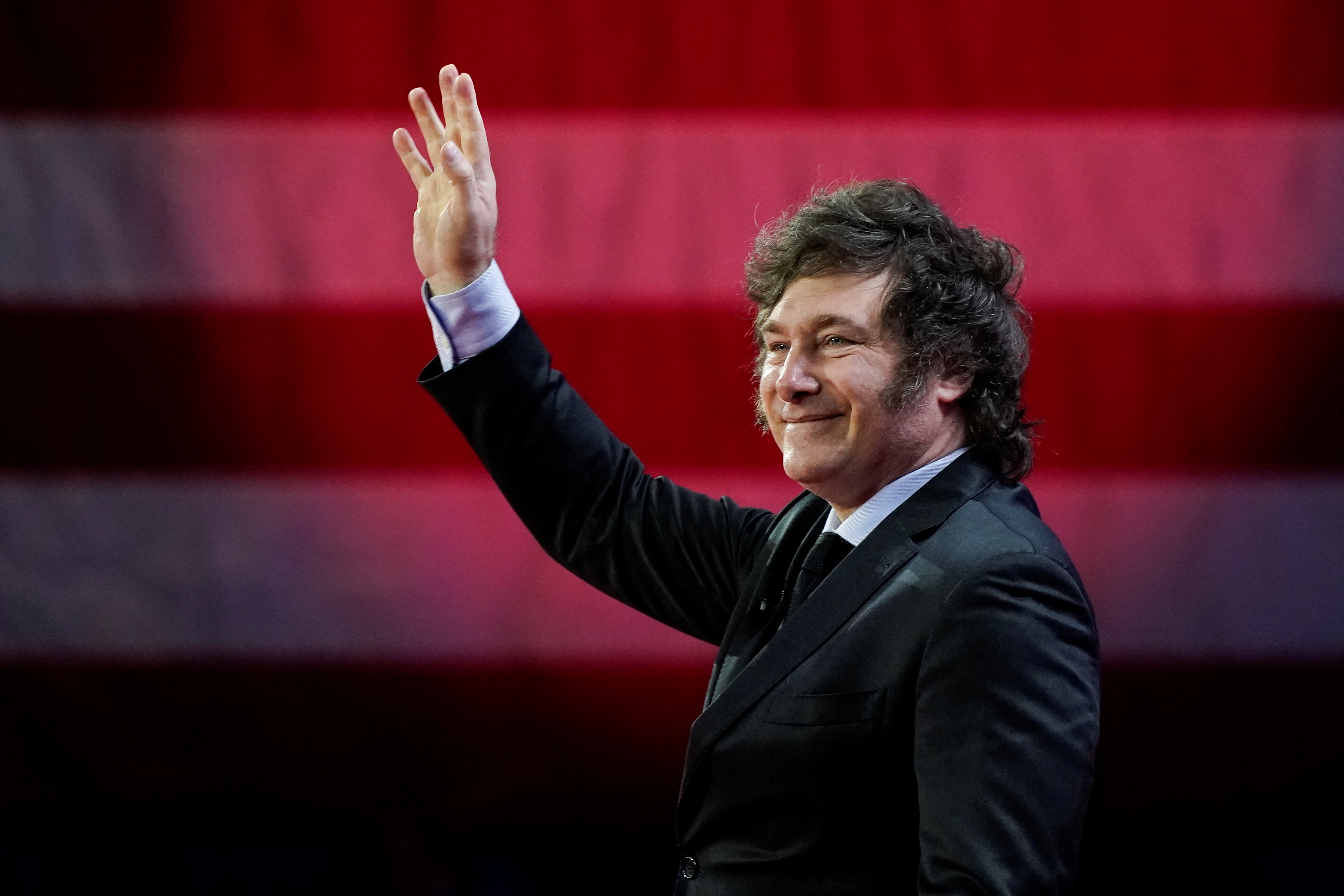 Javier Milei waves with a backdrop of a portion of the US flag