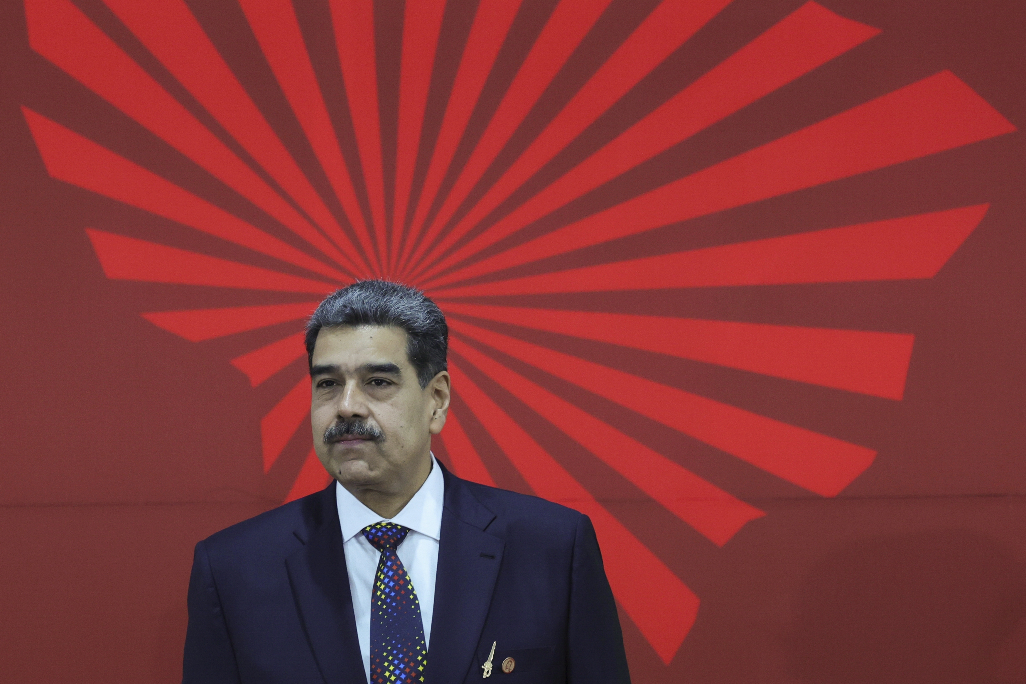 Venezuelan President Nicolas Maduro, standing in front of a mural of radiating lines in the shape of Venezuela