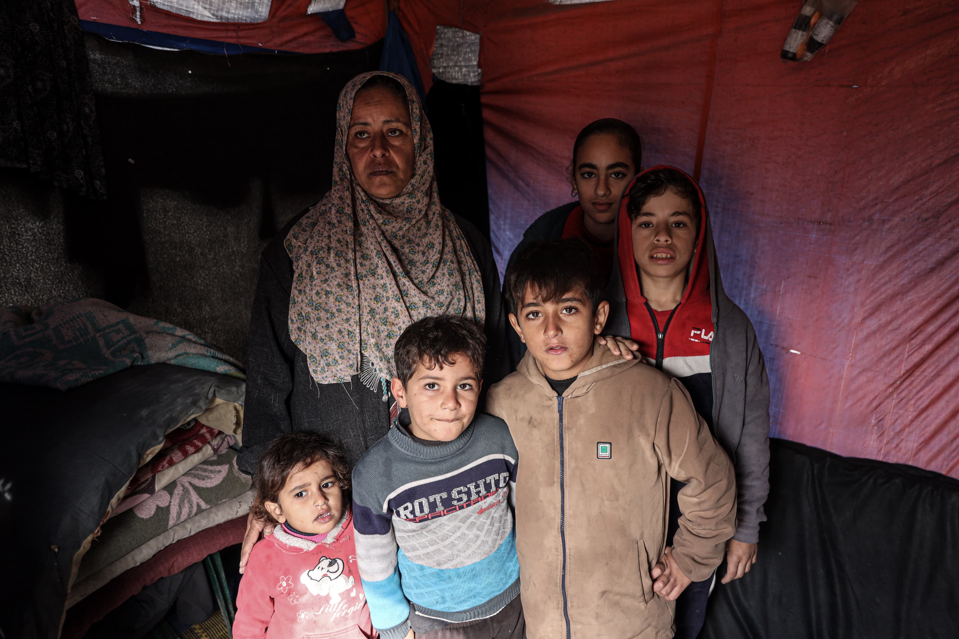Eman Shaghnoubi stands with her children inside their modest tent which has been soaked by the rain in Deir el-Balah, Gaza