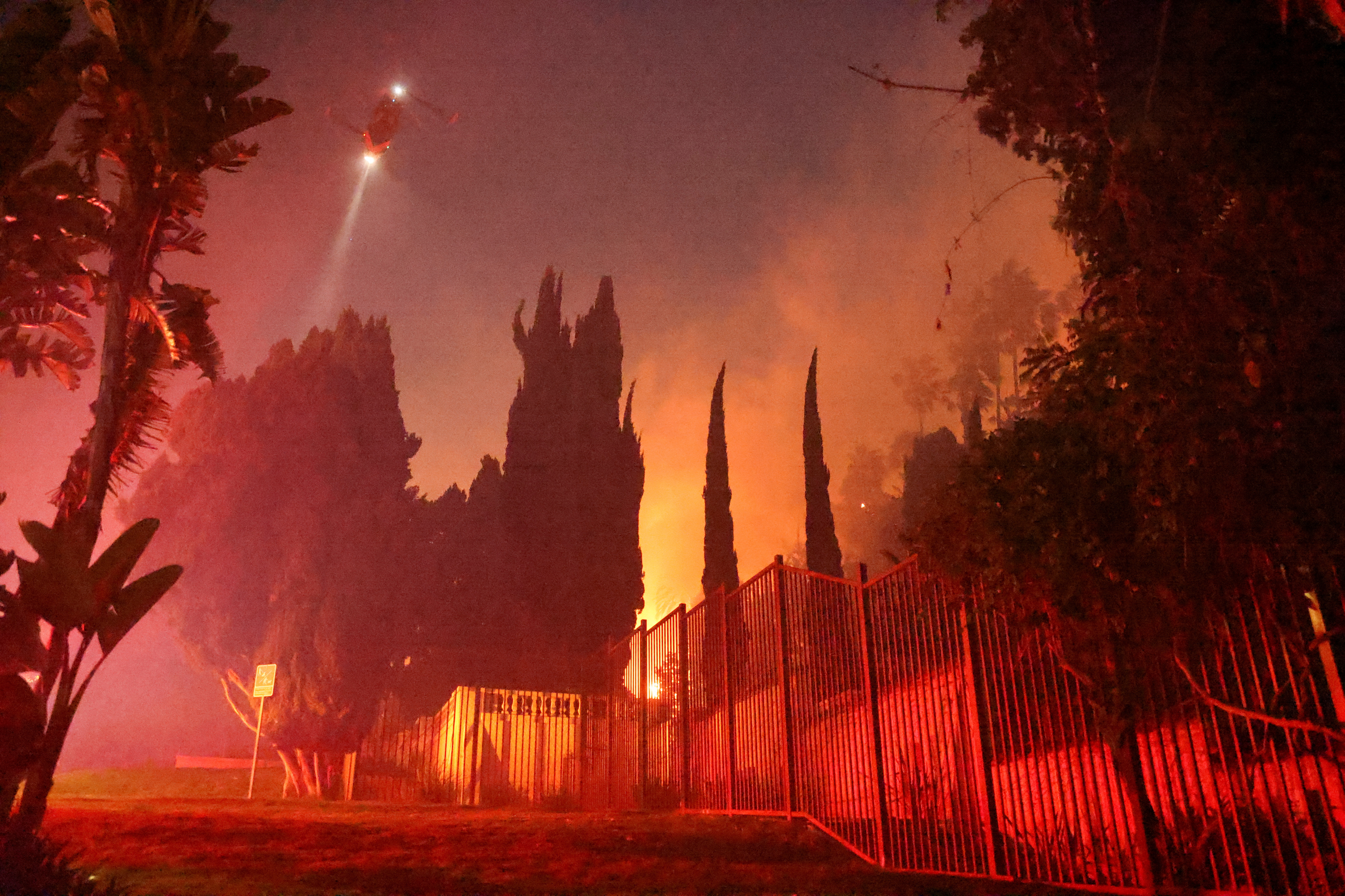 A helicopter flies as smoke rises from a fire in the hills.