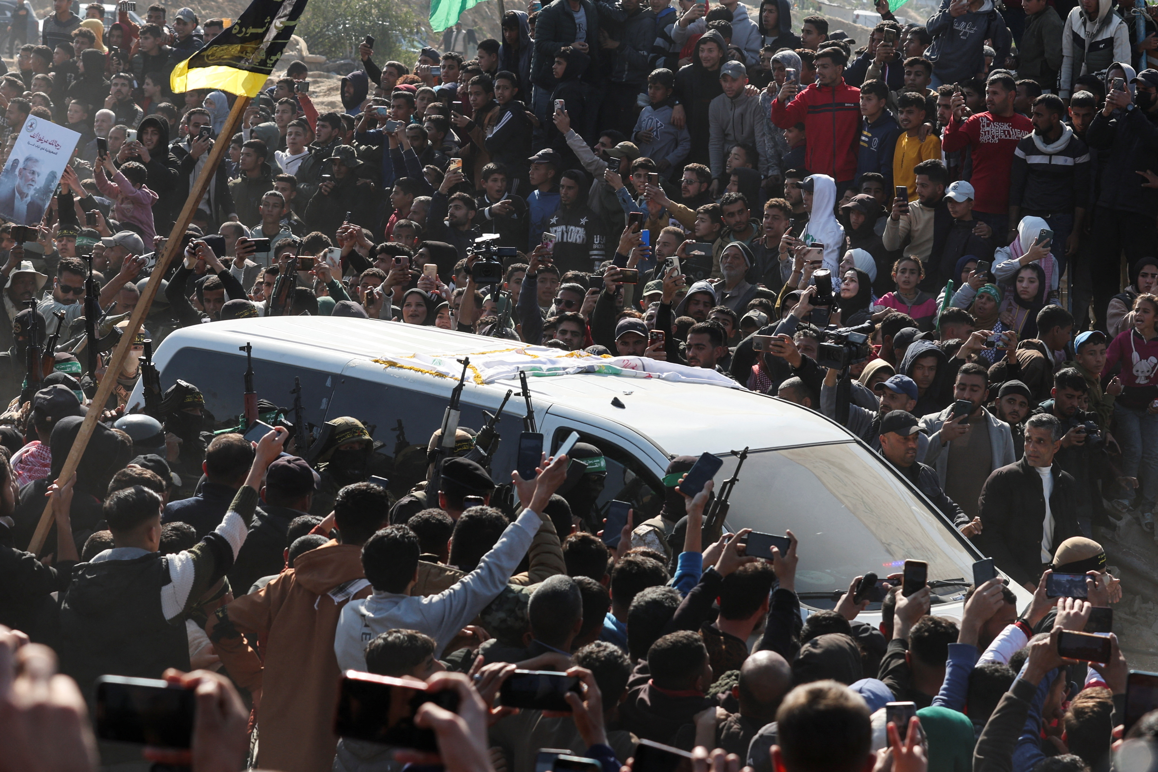 Palestinian fighters carry rifles next to a vehicle on the day they hand over captives held in Gaza since the Hamas-led October 7, 2023 attack on southern Israel, to members of the International Committee of the Red Cross