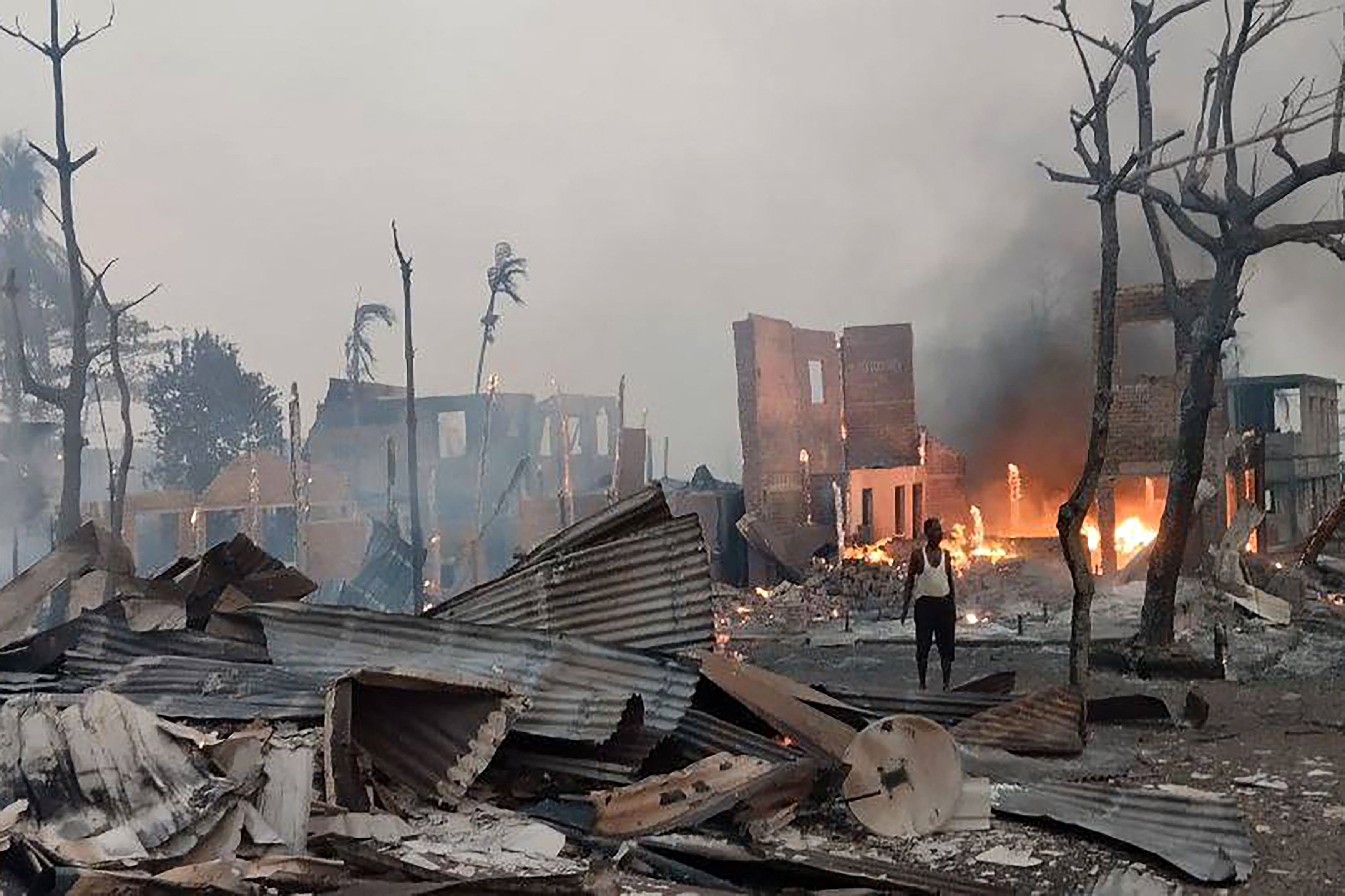 This handout photo taken and released on January 9, 2025 by the Arakan Army (AA) ethnic minority armed group shows a man standing near a burning house at the site of a suspected air strike carried out by Myanmar's military at Kyauk Ni Maw village in Ramree island in western Rakhine State. A Myanmar junta air strike killed at least 40 people in a town in western Rakhine state, a rescue worker and ethnic minority armed group told AFP on January 9, 2025. (Photo by Handout / Arakan Army (AA) / AFP) / -----EDITORS NOTE --- RESTRICTED TO EDITORIAL USE - MANDATORY CREDIT "AFP PHOTO / ARAKAN ARMY (AA) " - NO MARKETING - NO ADVERTISING CAMPAIGNS - DISTRIBUTED AS A SERVICE TO CLIENTS