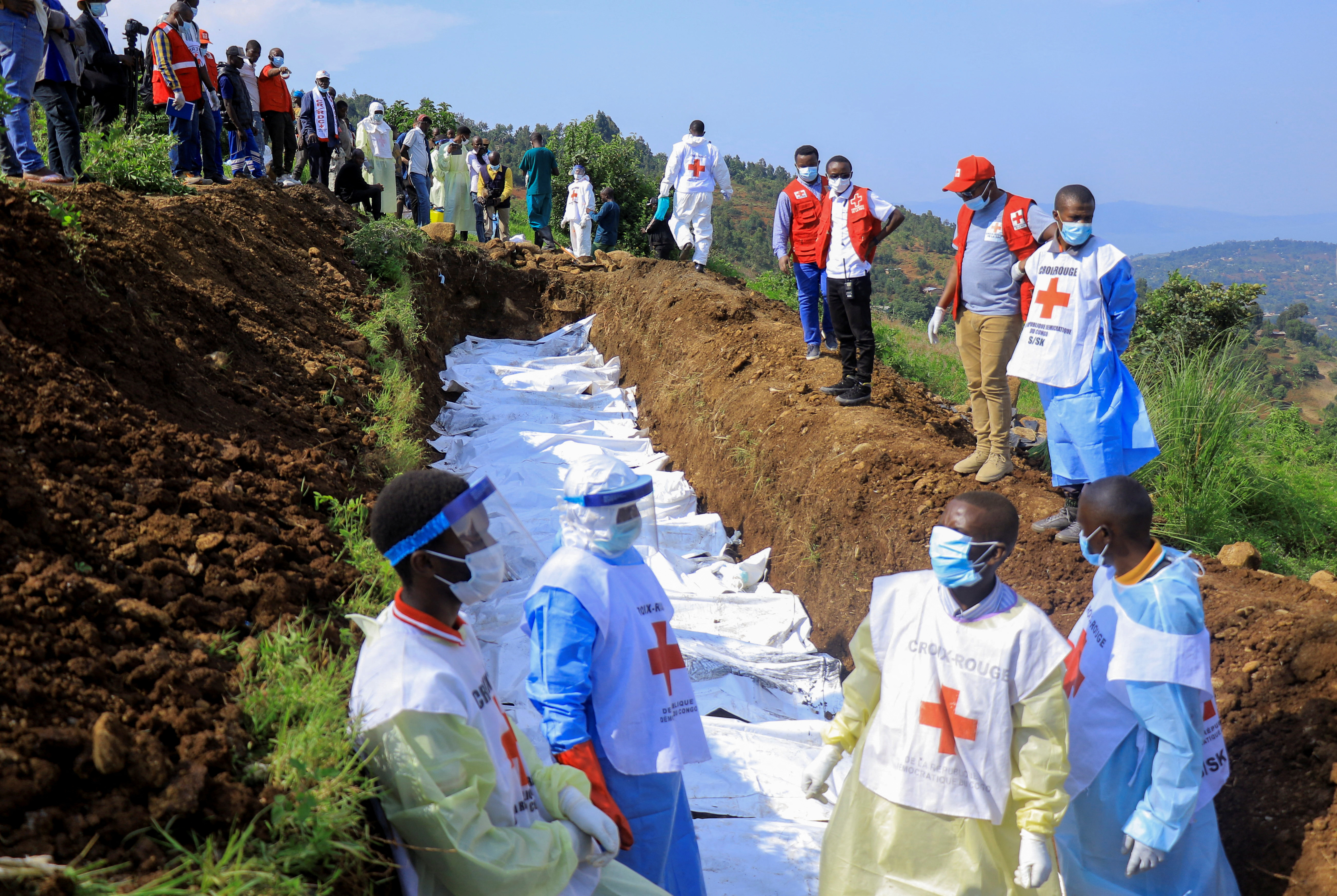 Congolese Red Cross members bury the body bags of victims in a mass grave.
