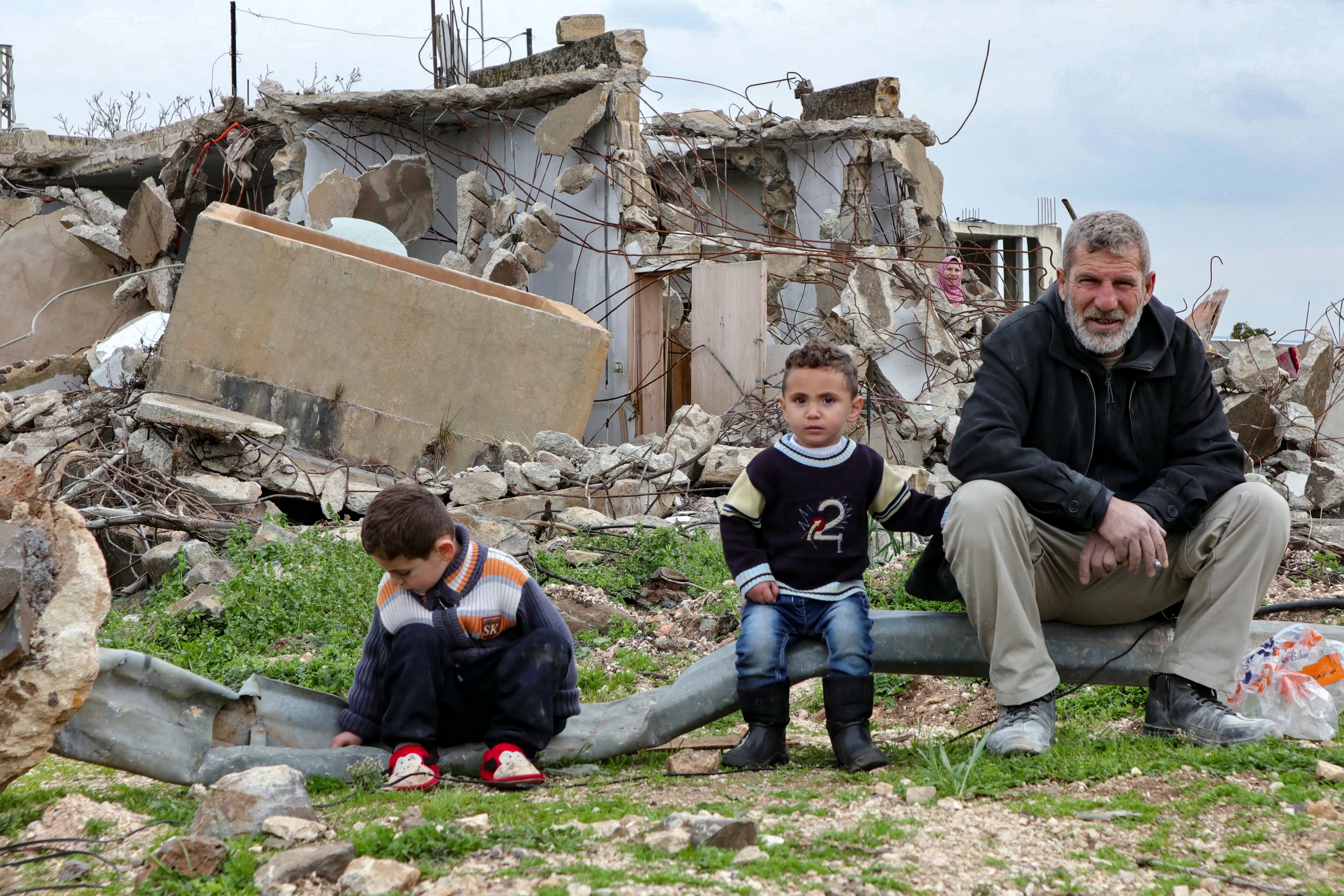 A family sit in front of a destroyed home.
