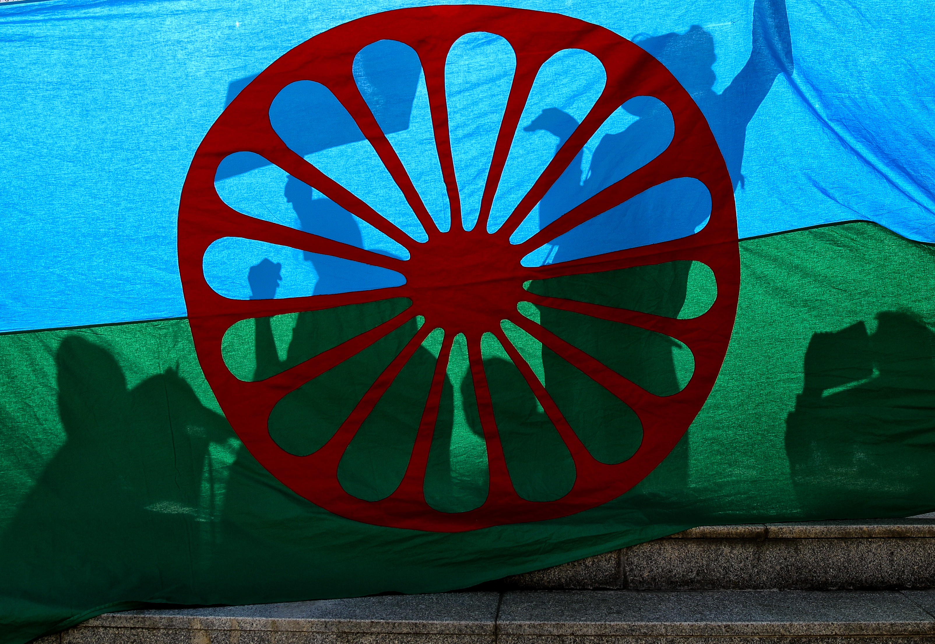 People cast shadows on the Roma flag during an anti-racism march by members of the Romanian Roma community celebrating the Romani Resistance Day in Bucharest, Romania, Saturday, May 18, 2019. On May 16, 1944 Roma prisoners in the Auschwitz concentration camp resisted an attempt by the Nazi troops to liquidate their camp, which postponed the action until August the same year. (AP Photo/Vadim Ghirda)