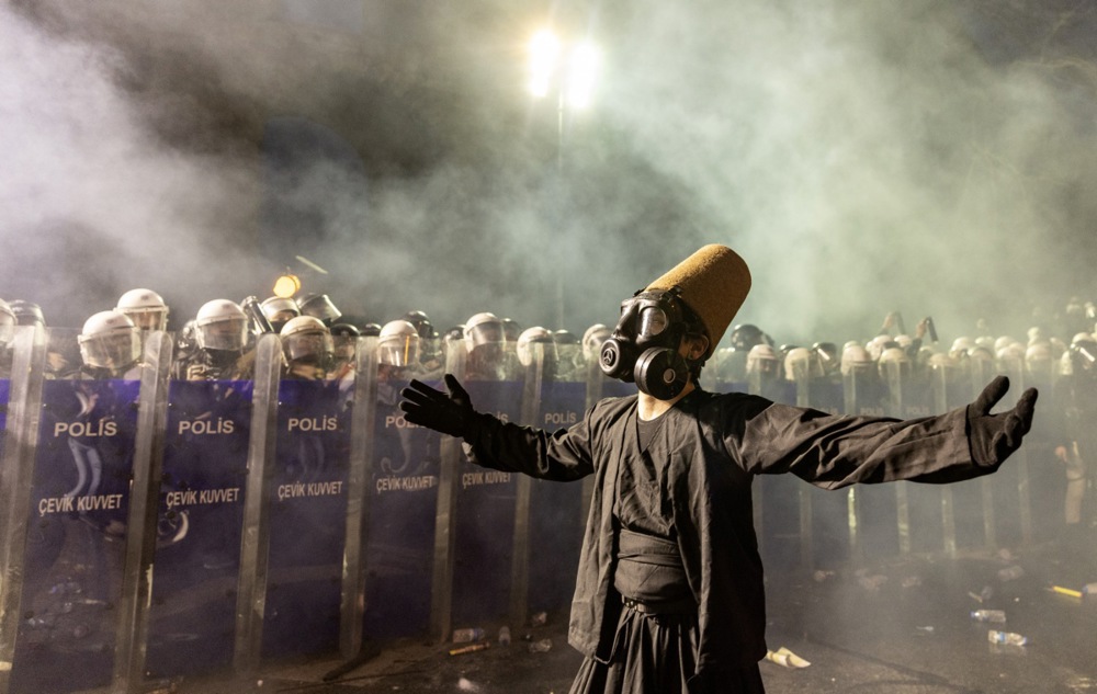 A protester wearing a whirling dervish costume performs in front of Turkish riot police barricades.