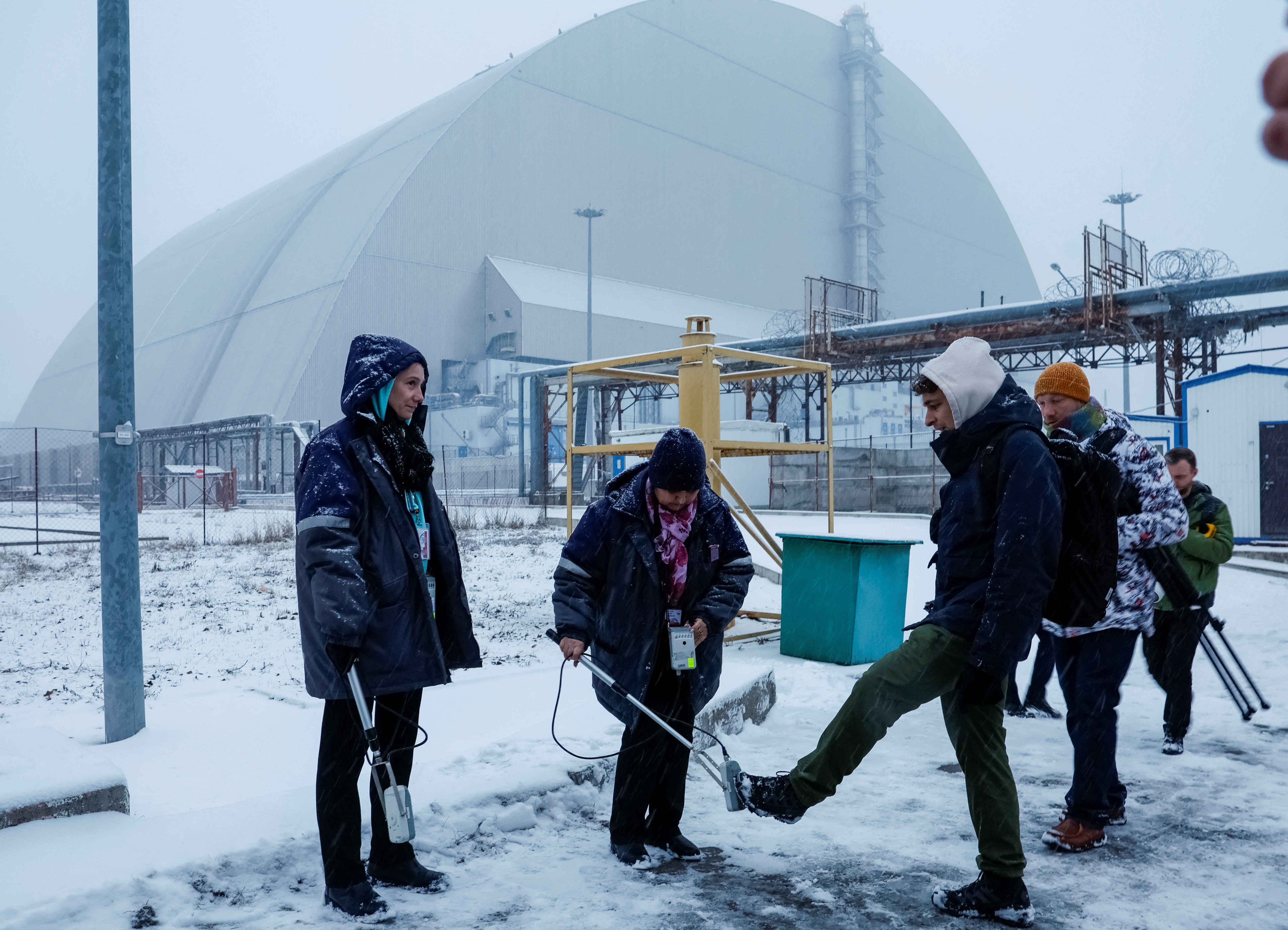 Journalists are seen during dosimetric control as they work near a New Safe Confinement (NSC) structure.
