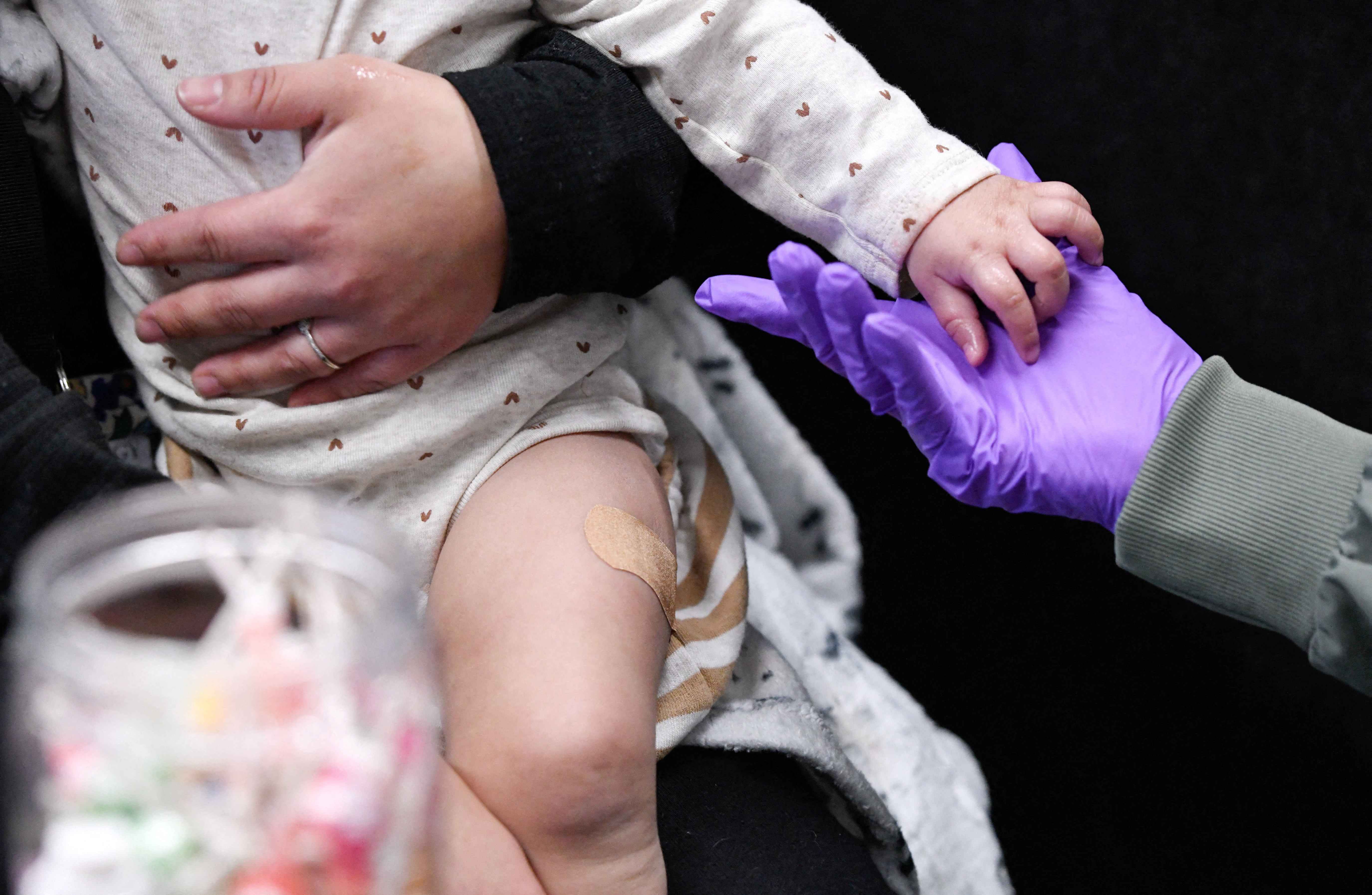 A healthcare provider holds a baby's hands while a parent holds the child in their lap.