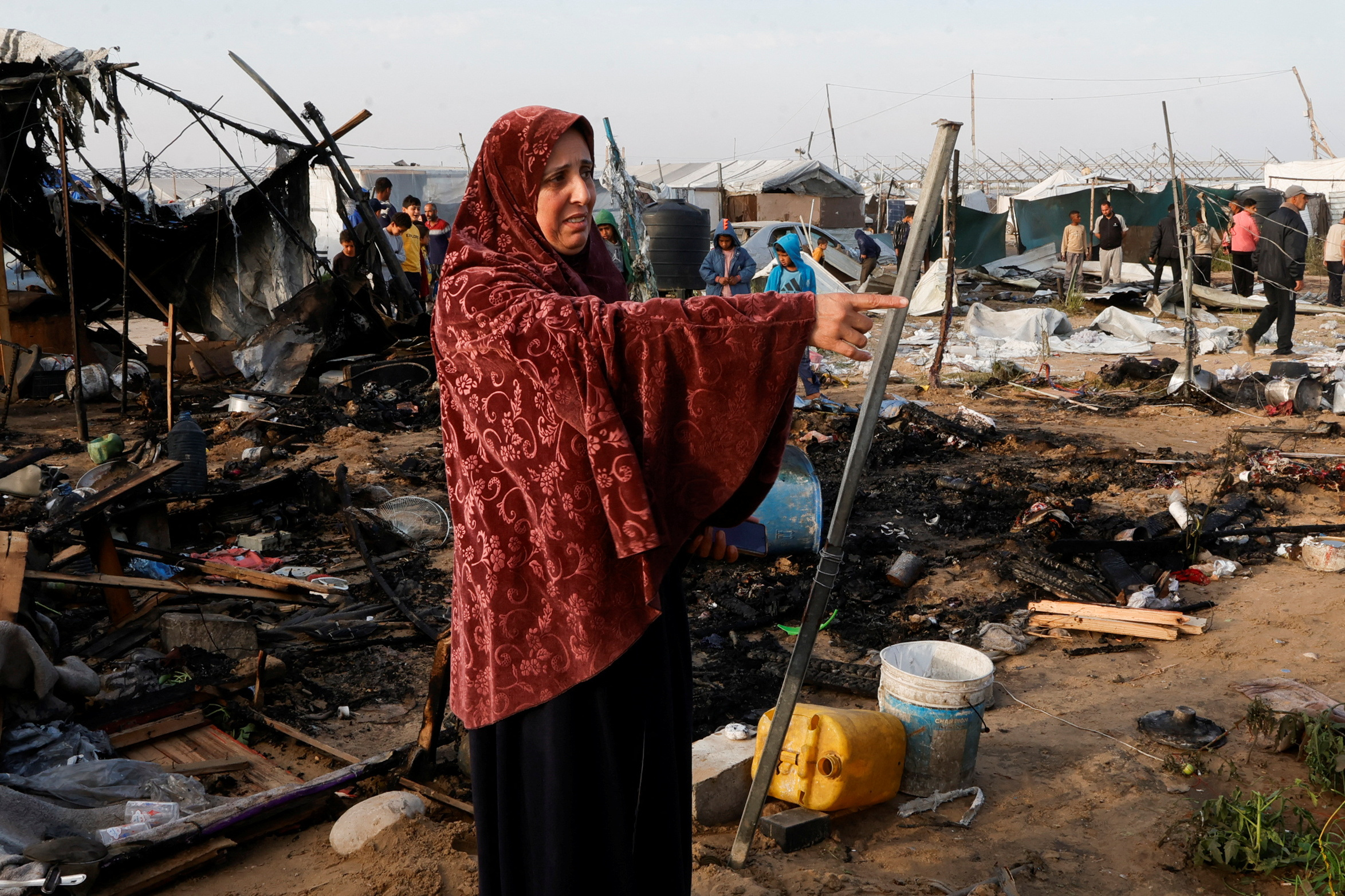A Palestinian woman gestures as people inspect the site of an Israeli strike on a tent camp housing displaced people, in the al-Mawasi designated ‘safe zone’, in Khan Younis in the southern Gaza Strip, on March 18, 2025