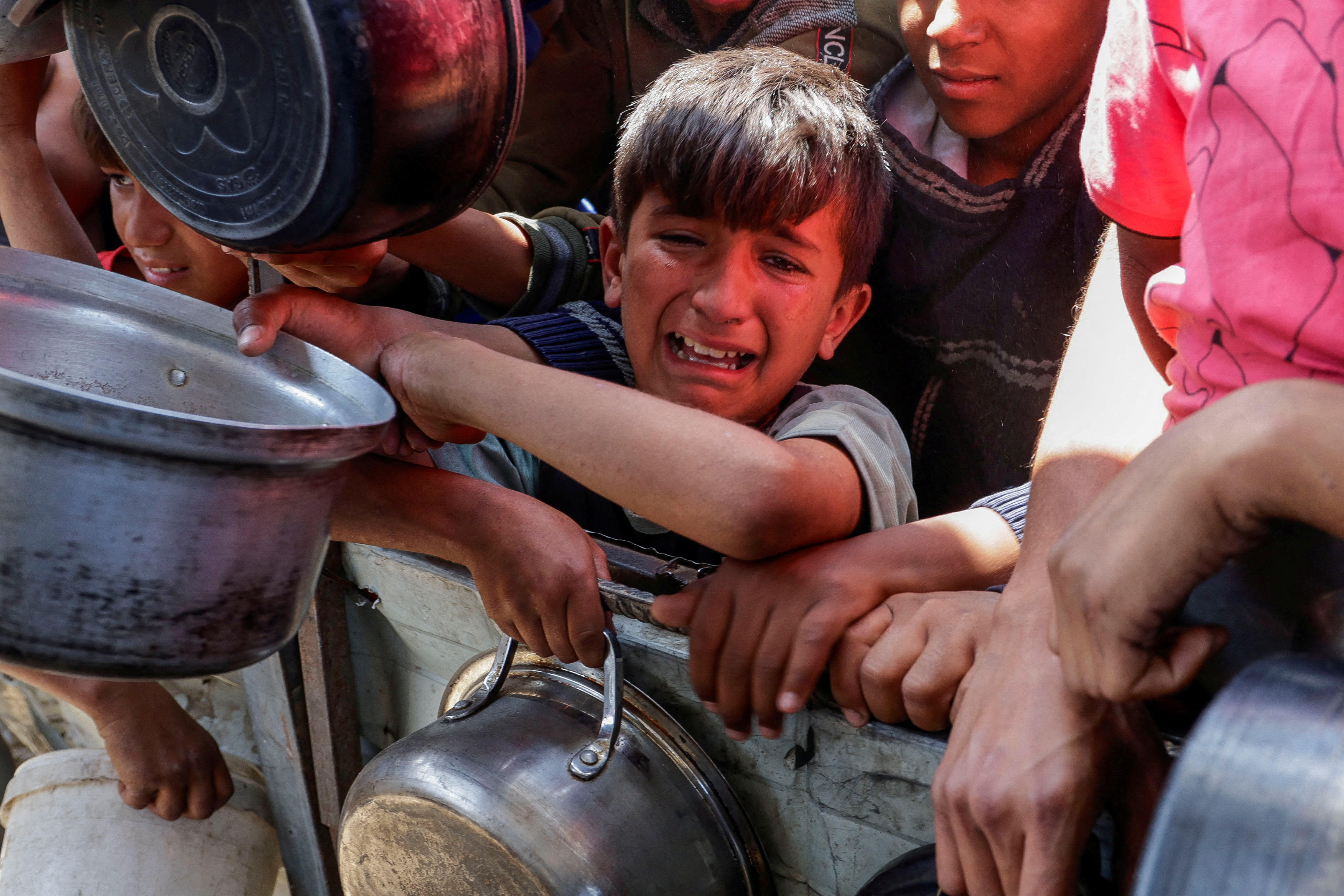 A Palestinian reacts as people gather to receive food cooked by a charity kitchen, in Khan Younis, southern Gaza Strip, April 29, 2025