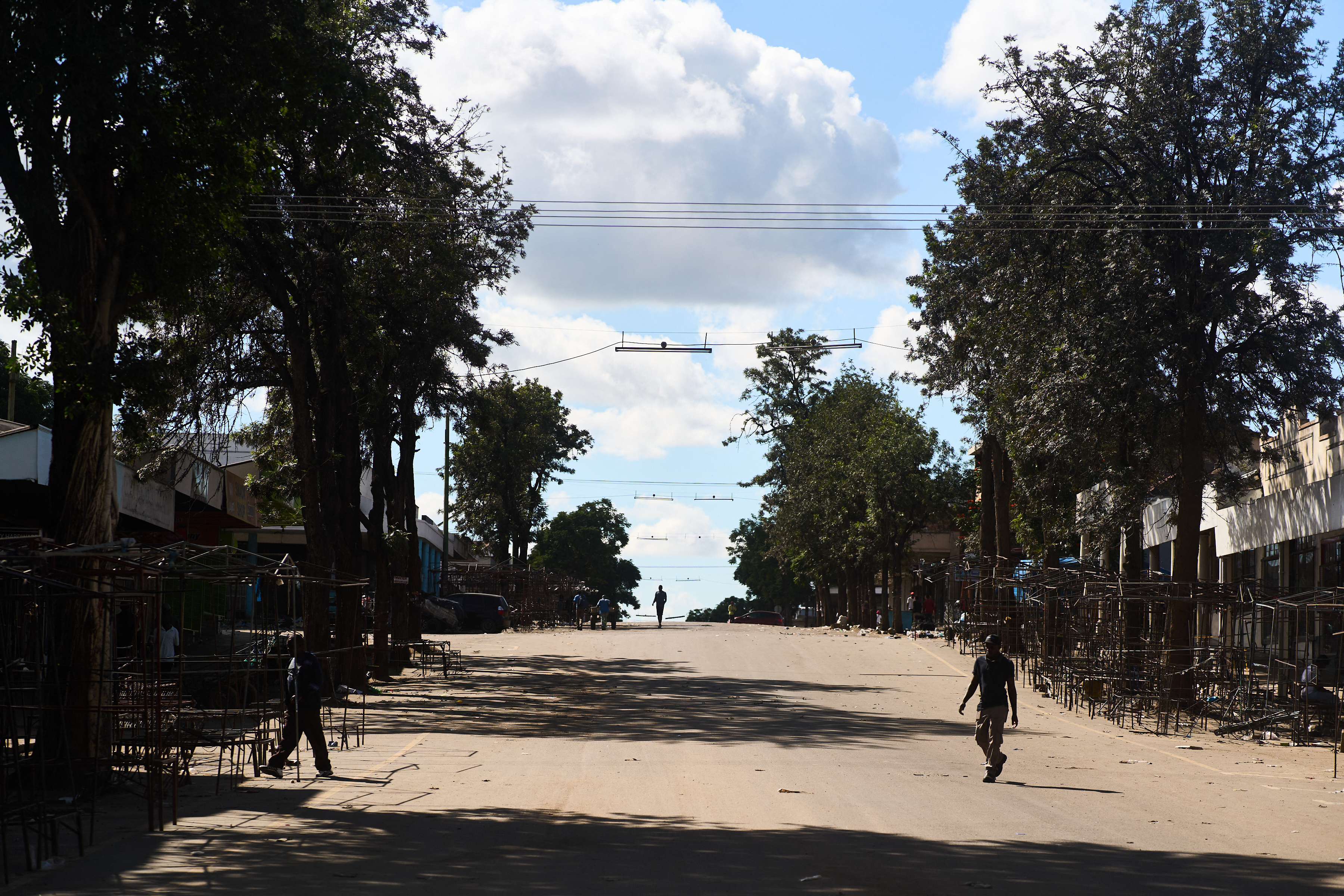 People walk past empty vending stalls along a deserted street in Bulawayo on March 31, 2025. Protests were called by a veteran of the ZANU-PF, in power since independence in 1980, following moves by a faction of the party to keep President Emmerson Mnangagwa, 82, in power beyond the end of his term in 2028