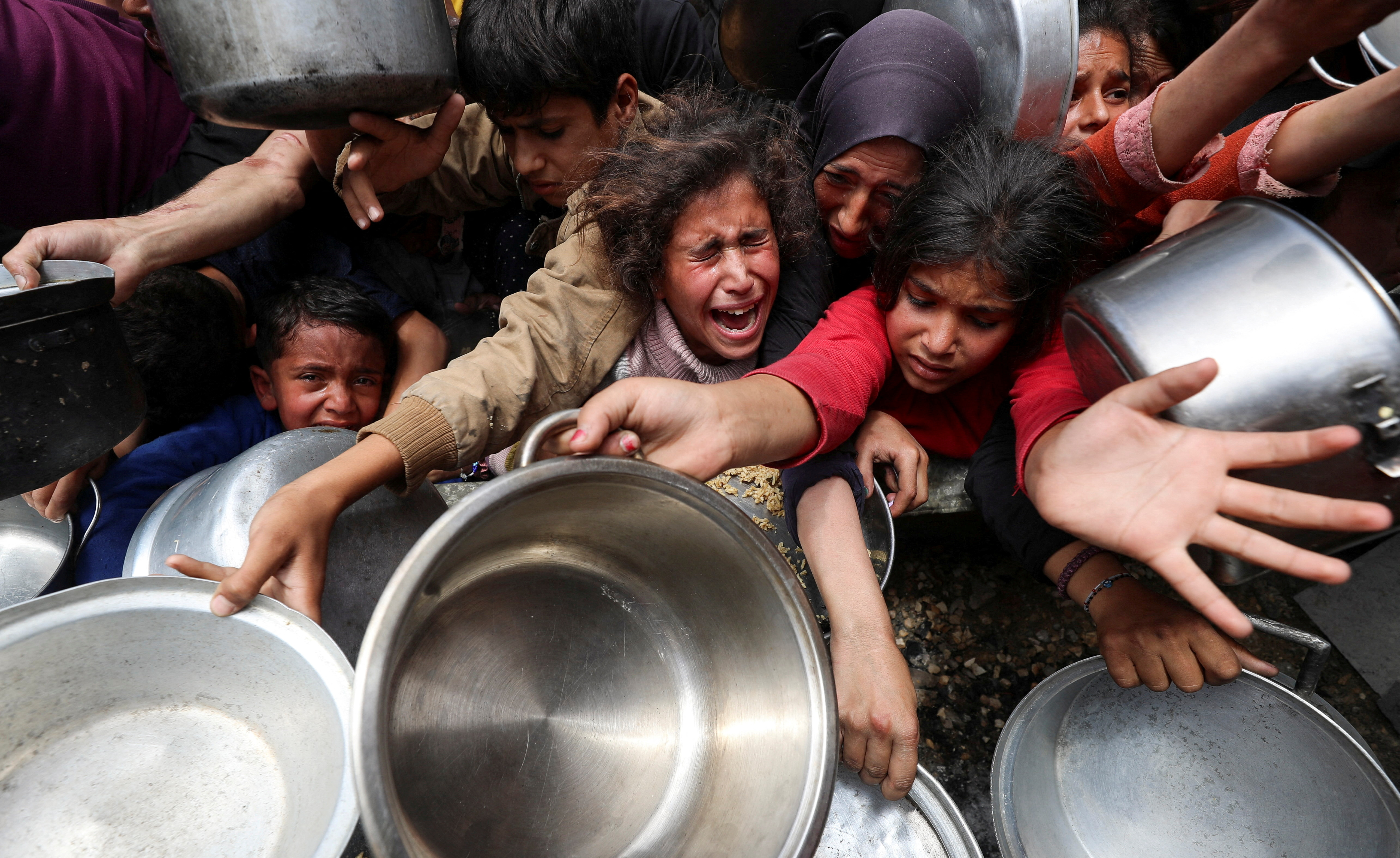 Palestinians wait to receive food cooked in Gaza