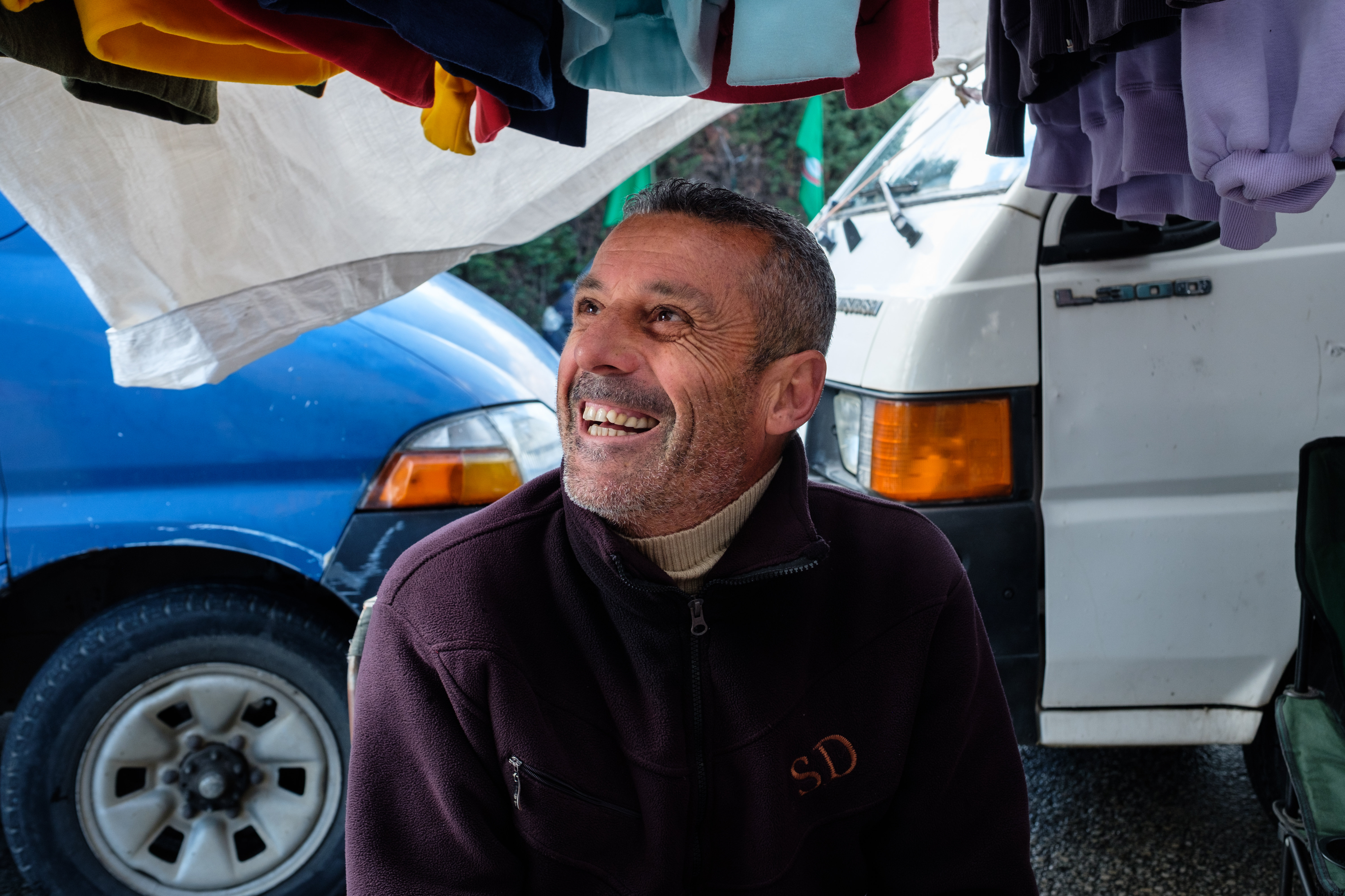Abbas Sbeity sits in front of his wares and van, grinning up to the side