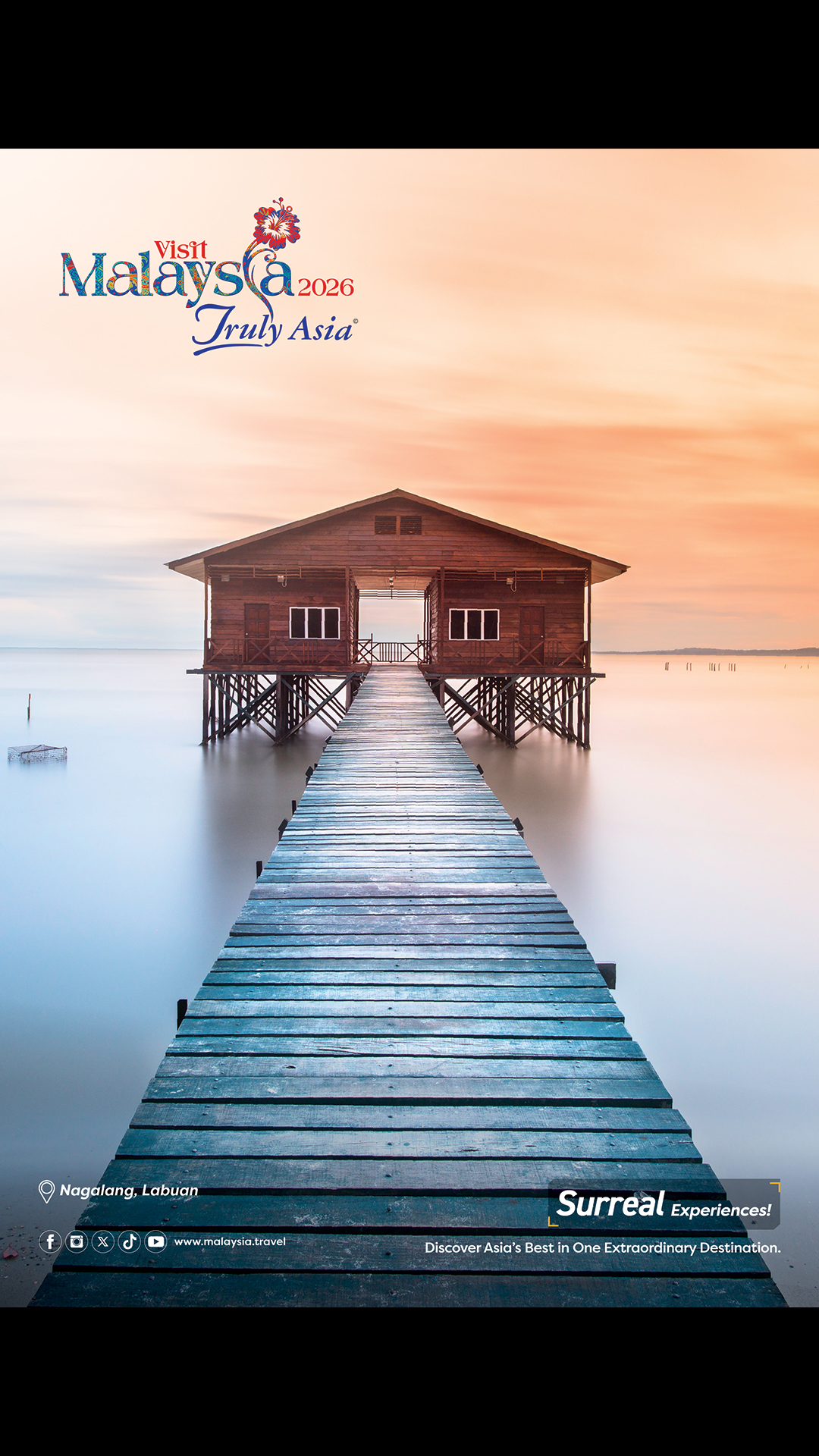 A wooden walkway over the water leads to a wooden building on stilts