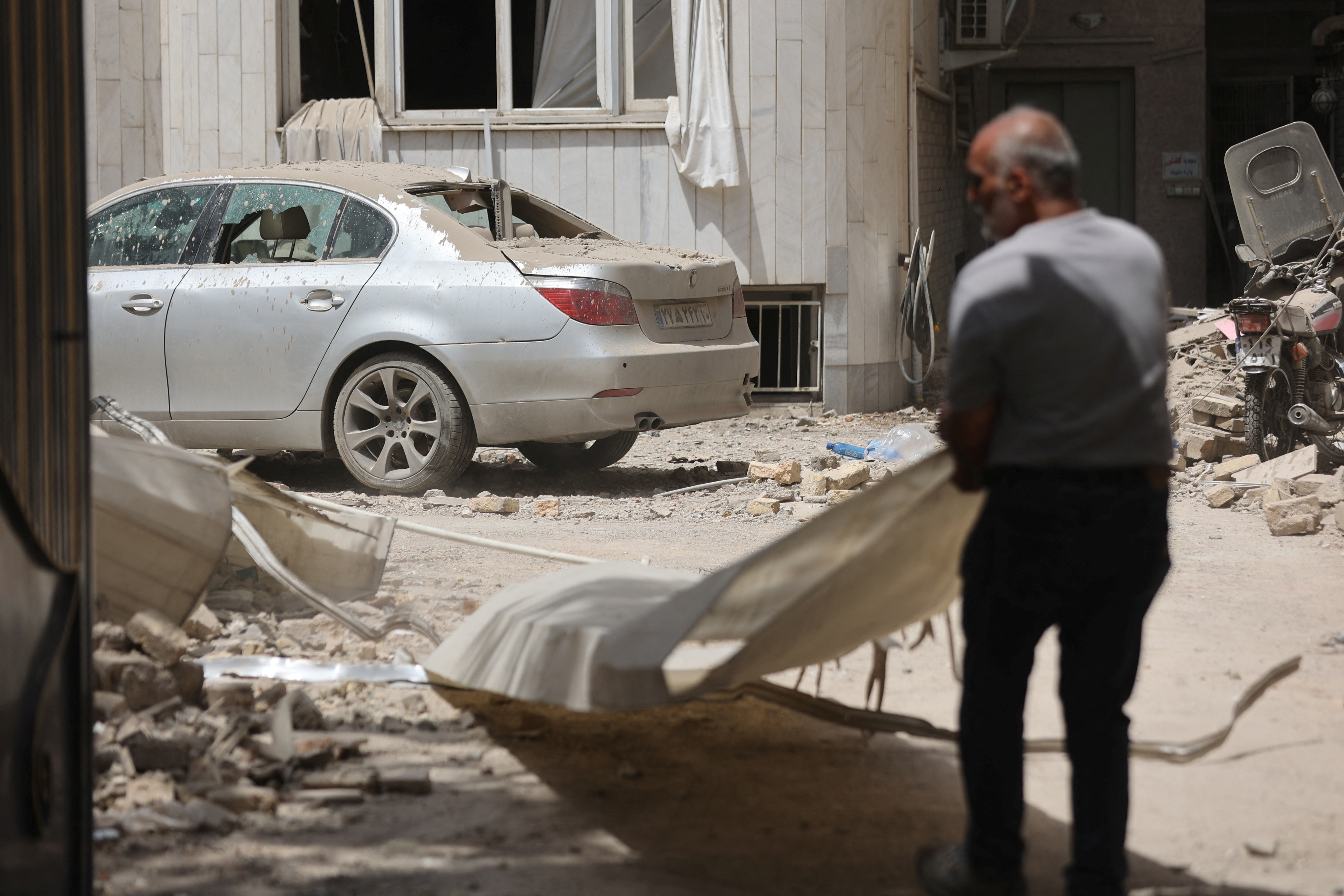 A man stands near a damaged car in Tehran, following an Israeli strike, June 26, 2025
