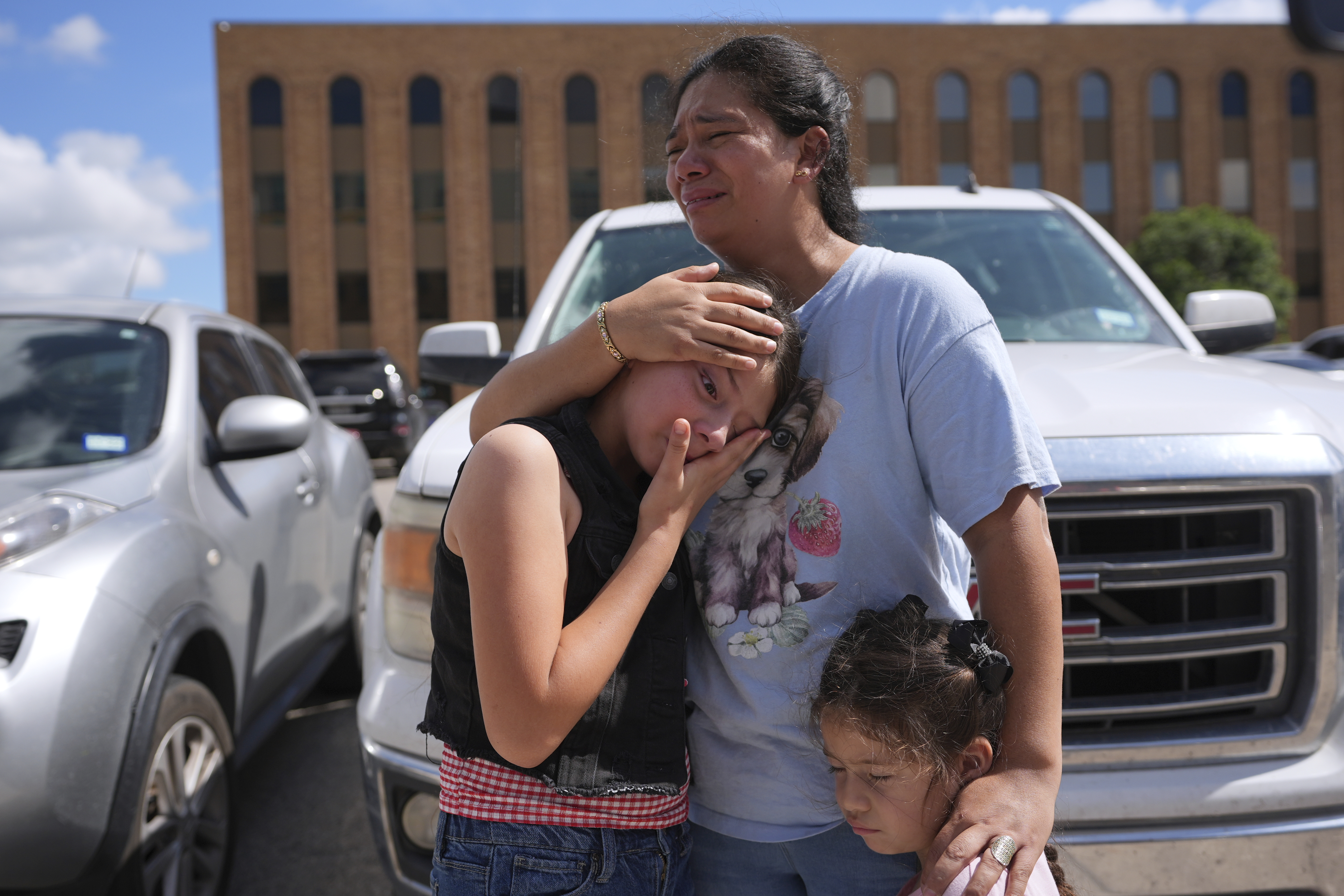 A mother comforts her crying children, holding them close to her body as they stand in the parking lot outside of immigration court.