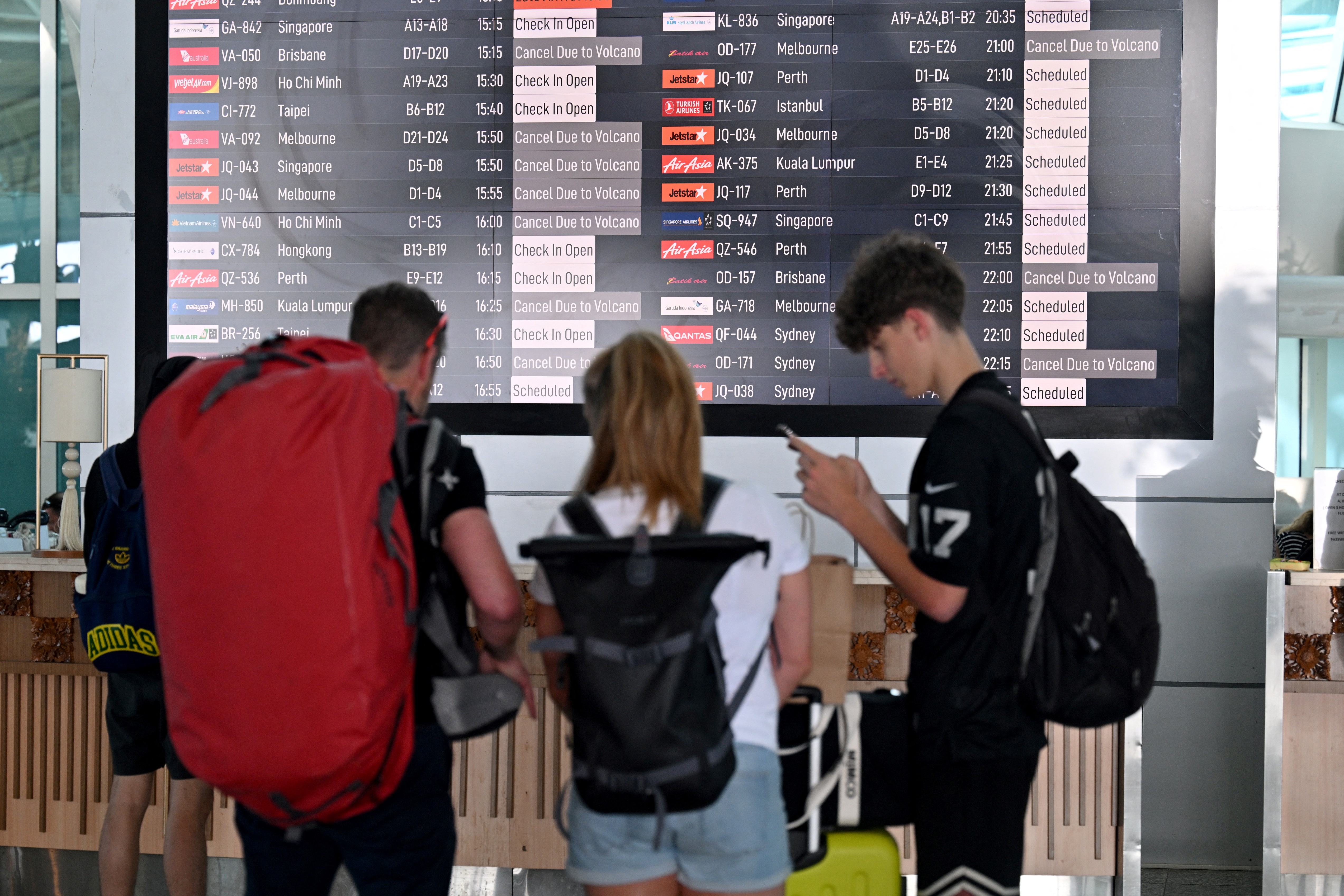 Passengers look at an electronic board displaying cancelled flights after the nearby Mount Lewotobi Laki-Laki volcano erupted, at Ngurah Rai International Airport in Tuban near Denpasar, on Indonesia's resort island of Bali on June 18, 2025.