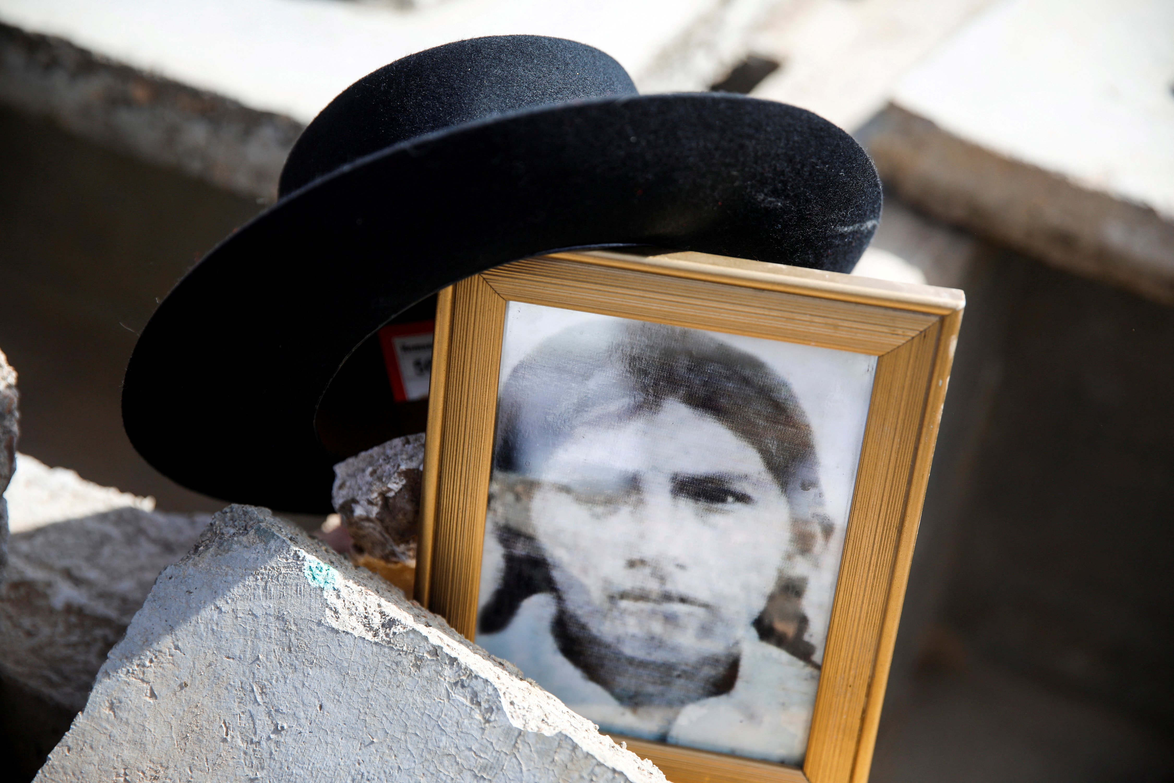 A framed, grainy black-and-white photo shows a victim of the Accomarca massacre. A black, wide-brimmed hat is balanced on a corner of the picture frame