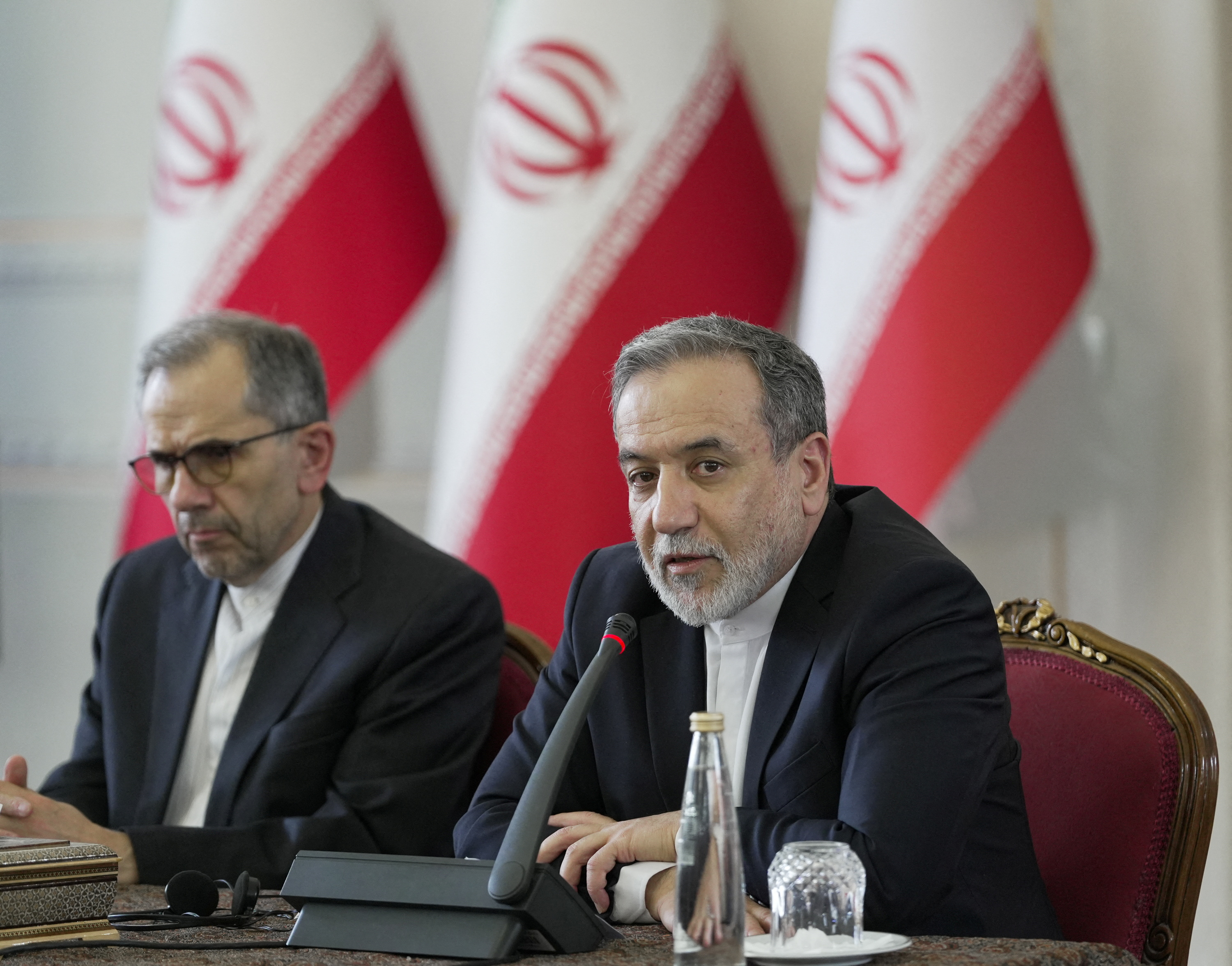 two men in suits sit in front of red and white flags