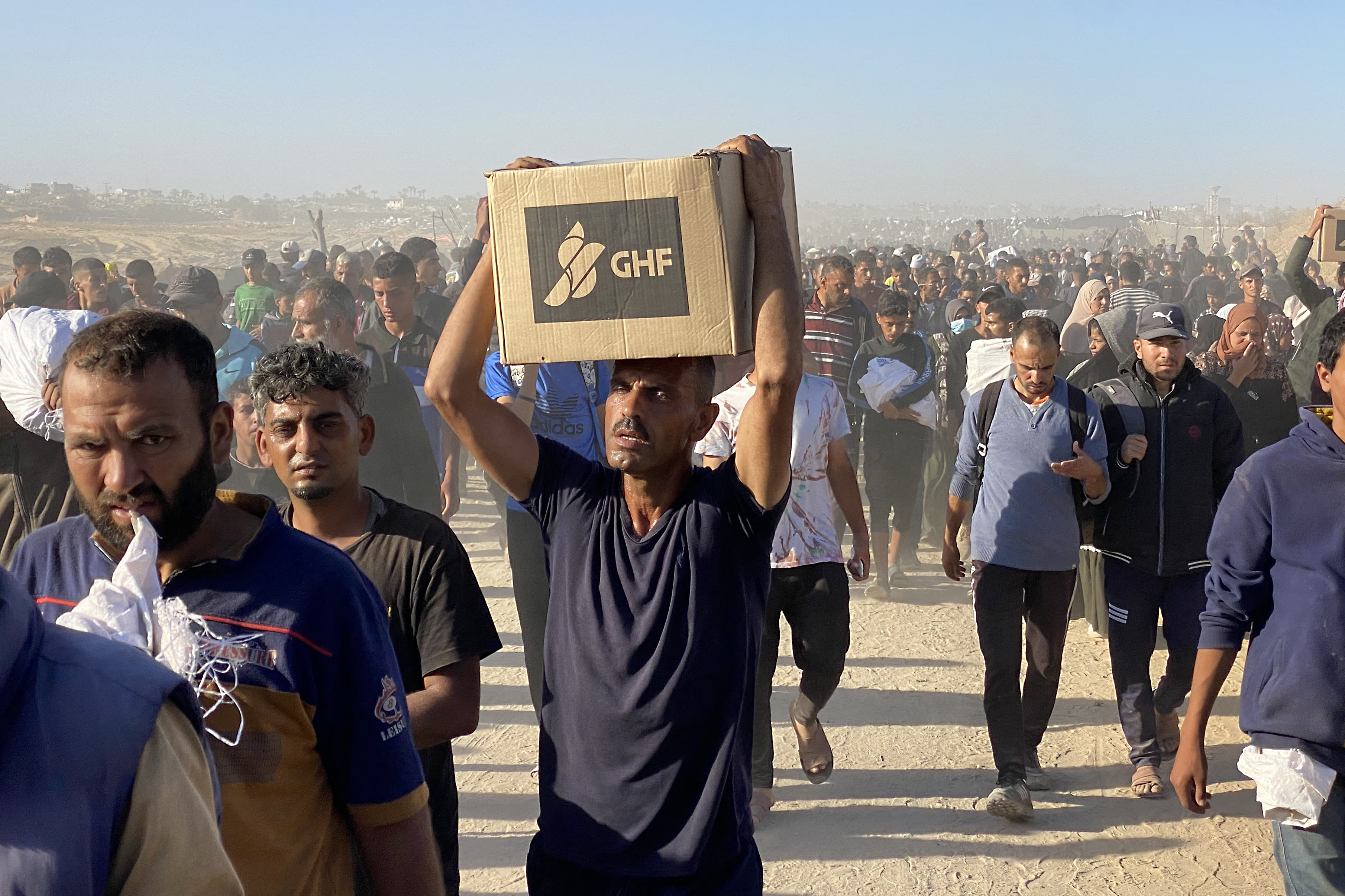 Displaced Palestinians carrying aid from a GHF hub in Rafah to their tents in May