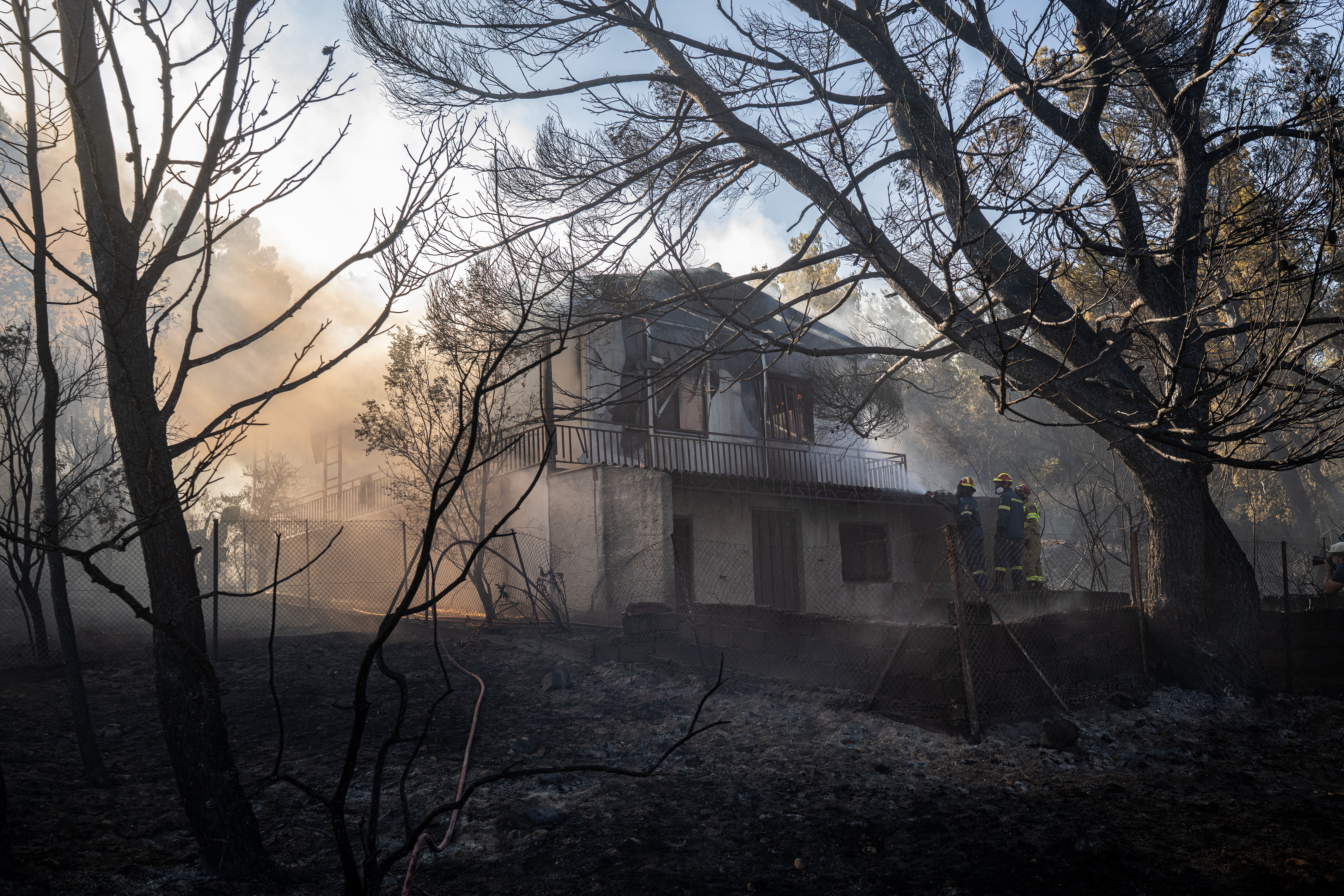 Firefighters spray water to douse a burning house in Pikermi