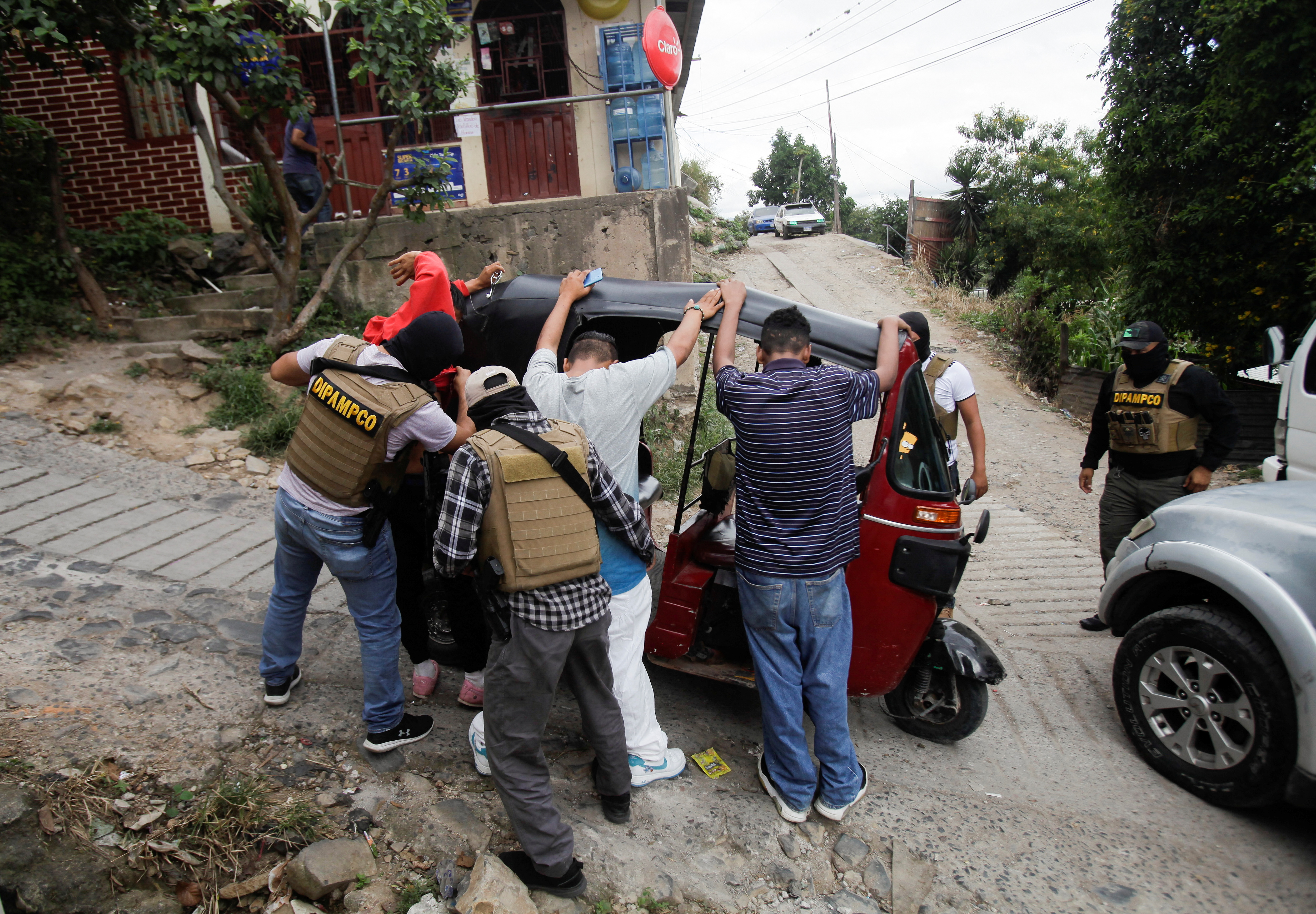 Members of DIPAMPCO inspect suspects who stand with hands raised against a vehicle.