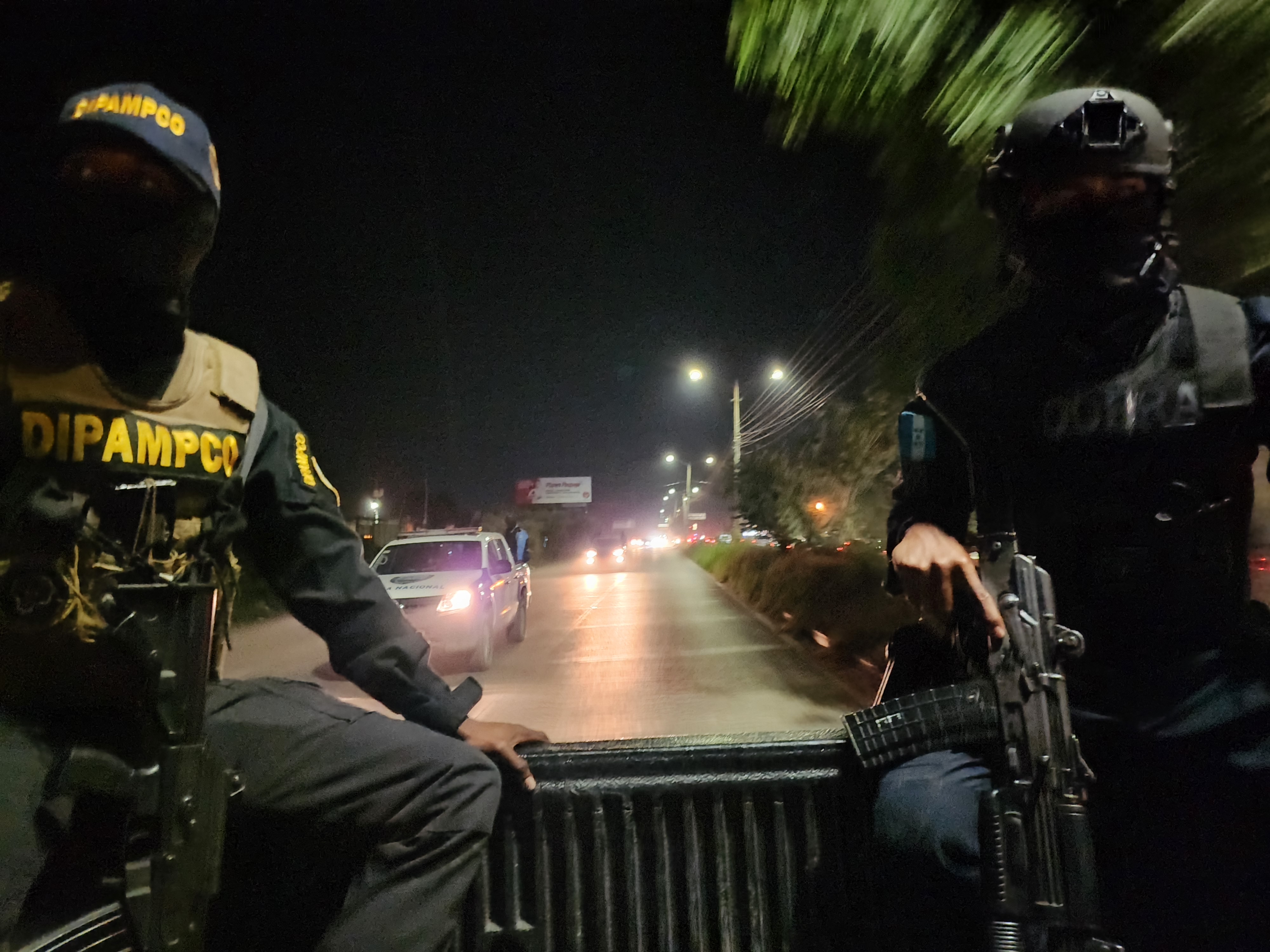 DIPAMPCO members, in bulletproof vests and helmets, ride in the back of a truck at nighttime.