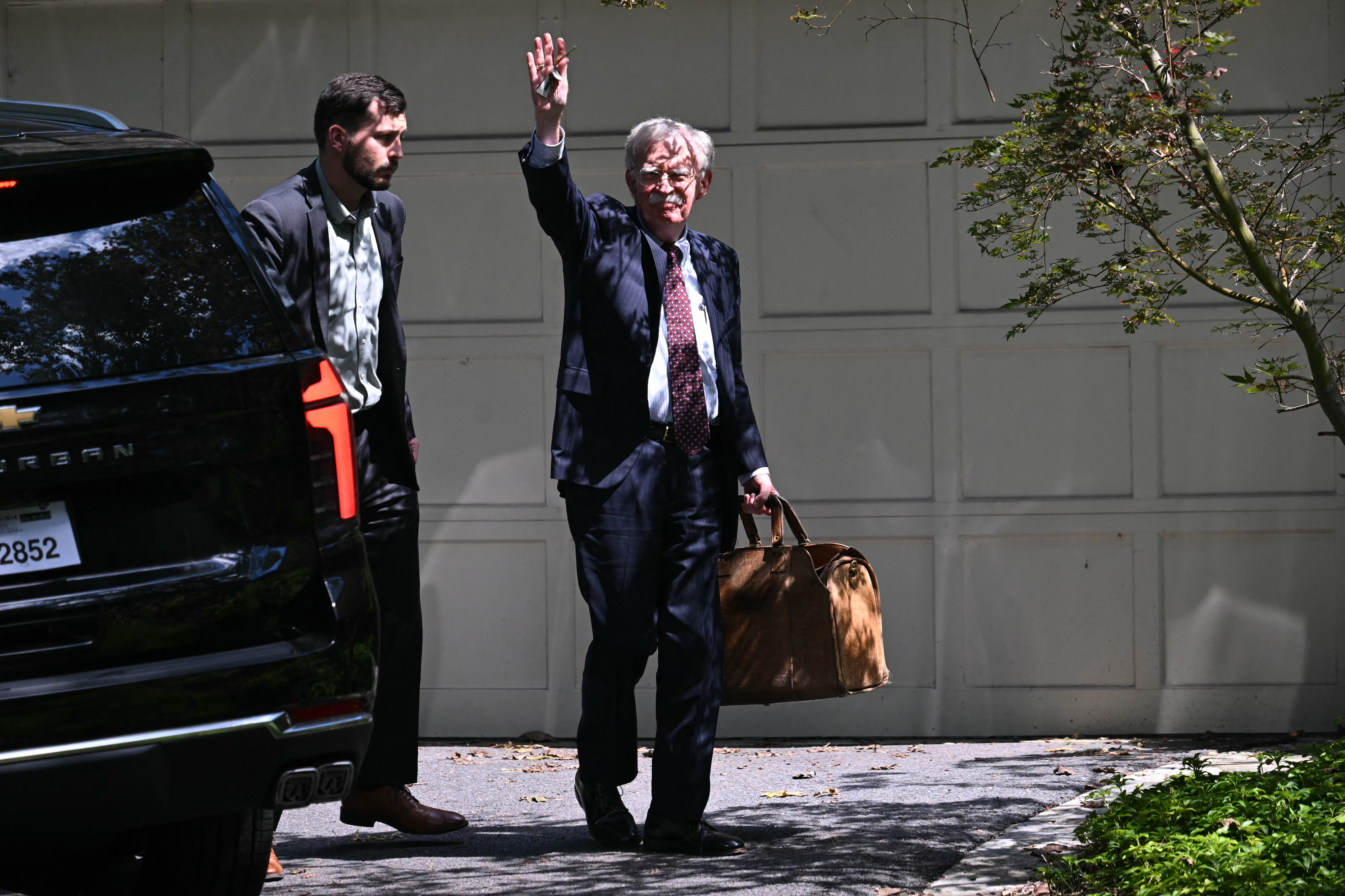 TOPSHOT - Donald Trump's former national security advisor John Bolton waves as he arrives his house, after the FBI conducted a court-authorized search at his place on August 22, 2025 in Bethesda, Maryland.
