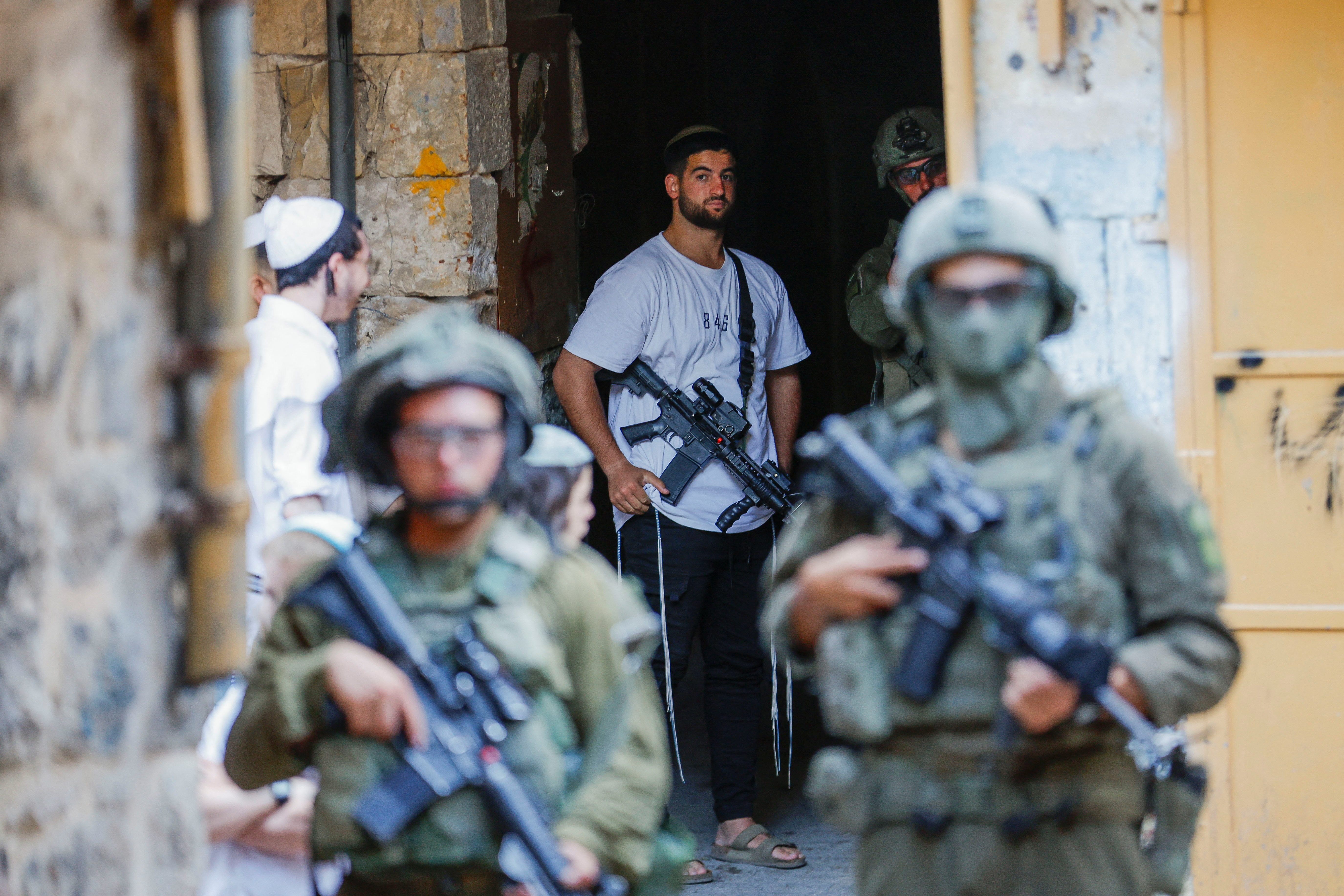 An armed settler stands near Israeli troops during a weekly settlers’ tour in Hebron, in the occupied West Bank, August 23, 2025