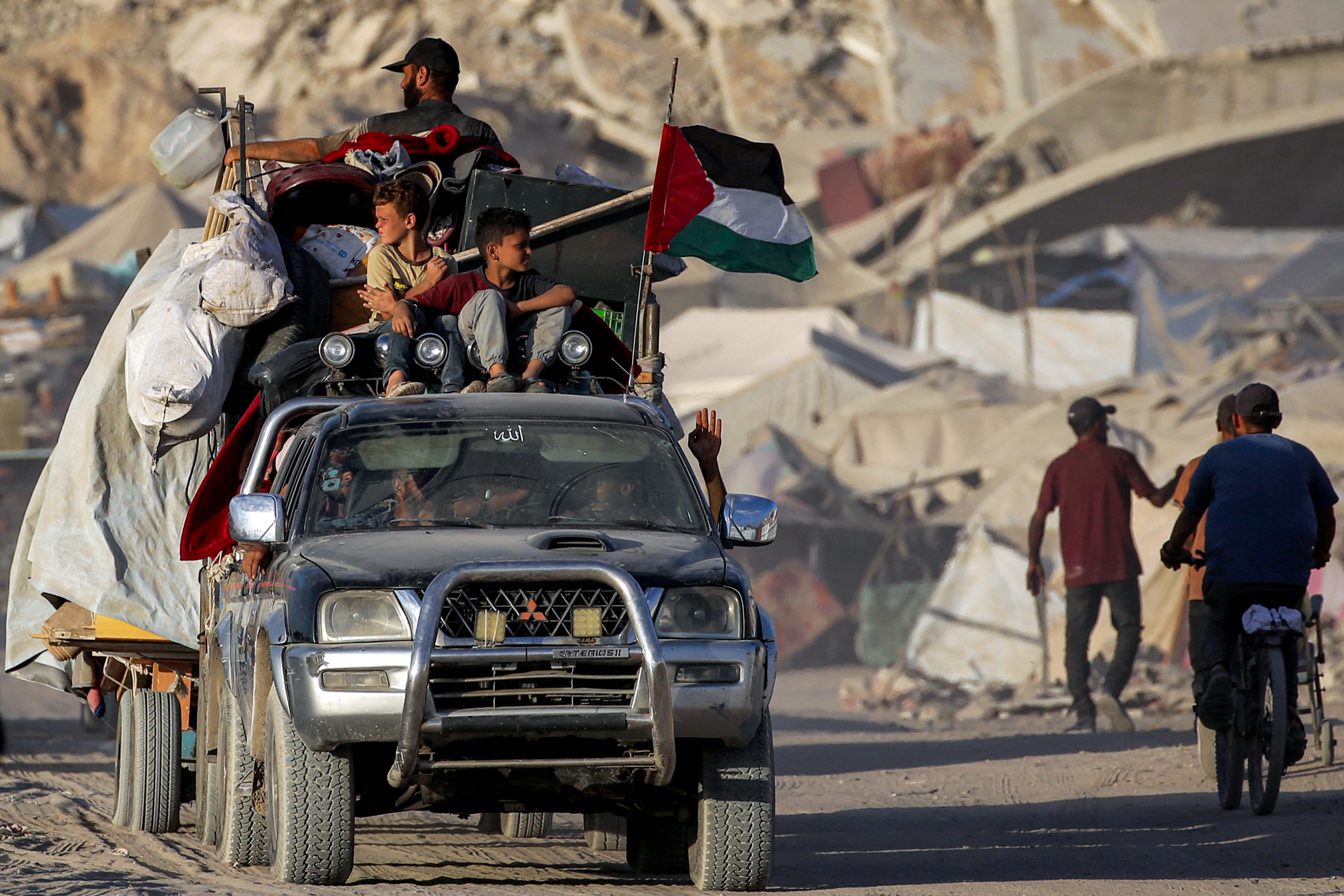 A Palestinian flag flies from a truck carrying people and children with their belongings