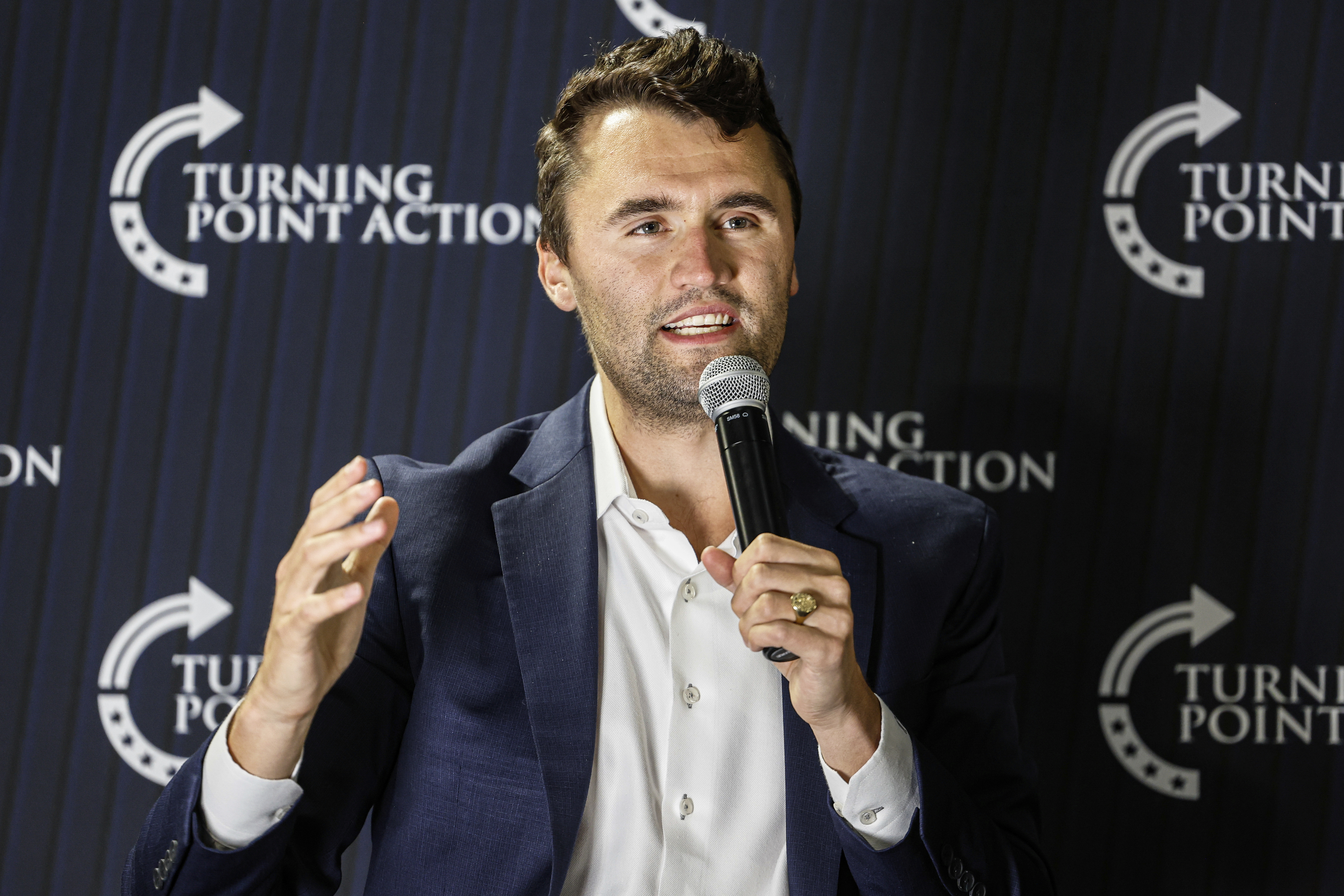 Charlie Kirk holds a microphone and speaks.
