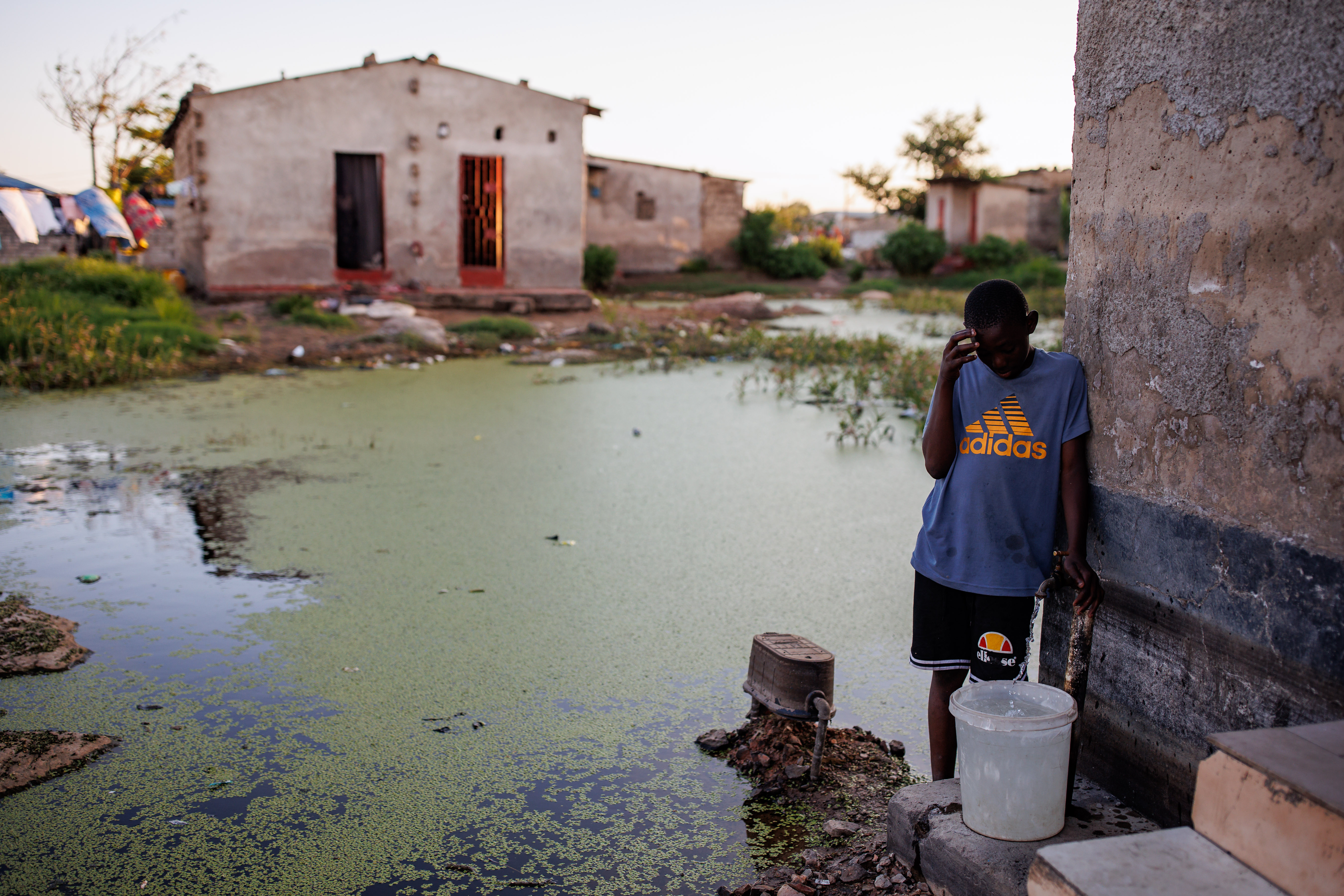 LUSAKA, ZAMBIA - FEBRUARY 24: A young boy fetches drinking water from a tap surrounded by contaminated water on February 24, 2024 in Lusaka, Zambia. Cholera, a waterborne bacterial disease, has unleashed a perilous wave across southern Africa, with active outbreaks currently afflicting five countries in southern and central Africa. Over the past two years, the epidemic has left a devastating trail, infecting more than 220,000 individuals, and claiming the lives of over 4,000 people in 19 countries across the continent. Public health experts attribute the widespread devastation to a confluence of factors, including increasingly intense storms driven by climate change, a shortage of vaccines, and inadequate water and sewer infrastructure. Among the affected nations, Zambia stands as one of the hardest hit, grappling with its deadliest cholera outbreak on record. Since October, the country has witnessed over 700 fatalities and more than 18,500 infections, although cases and deaths have shown signs of slowing since their peak in January. (Photo by Luke Dray/Getty Images)