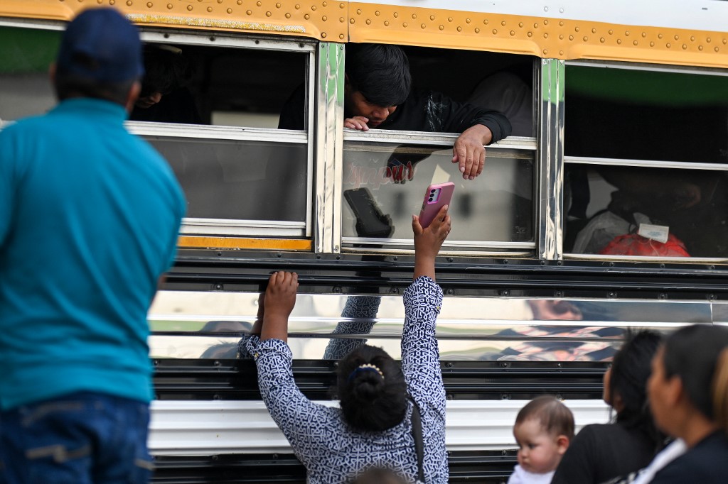 A woman shows a cellphone to a man inside a bus.