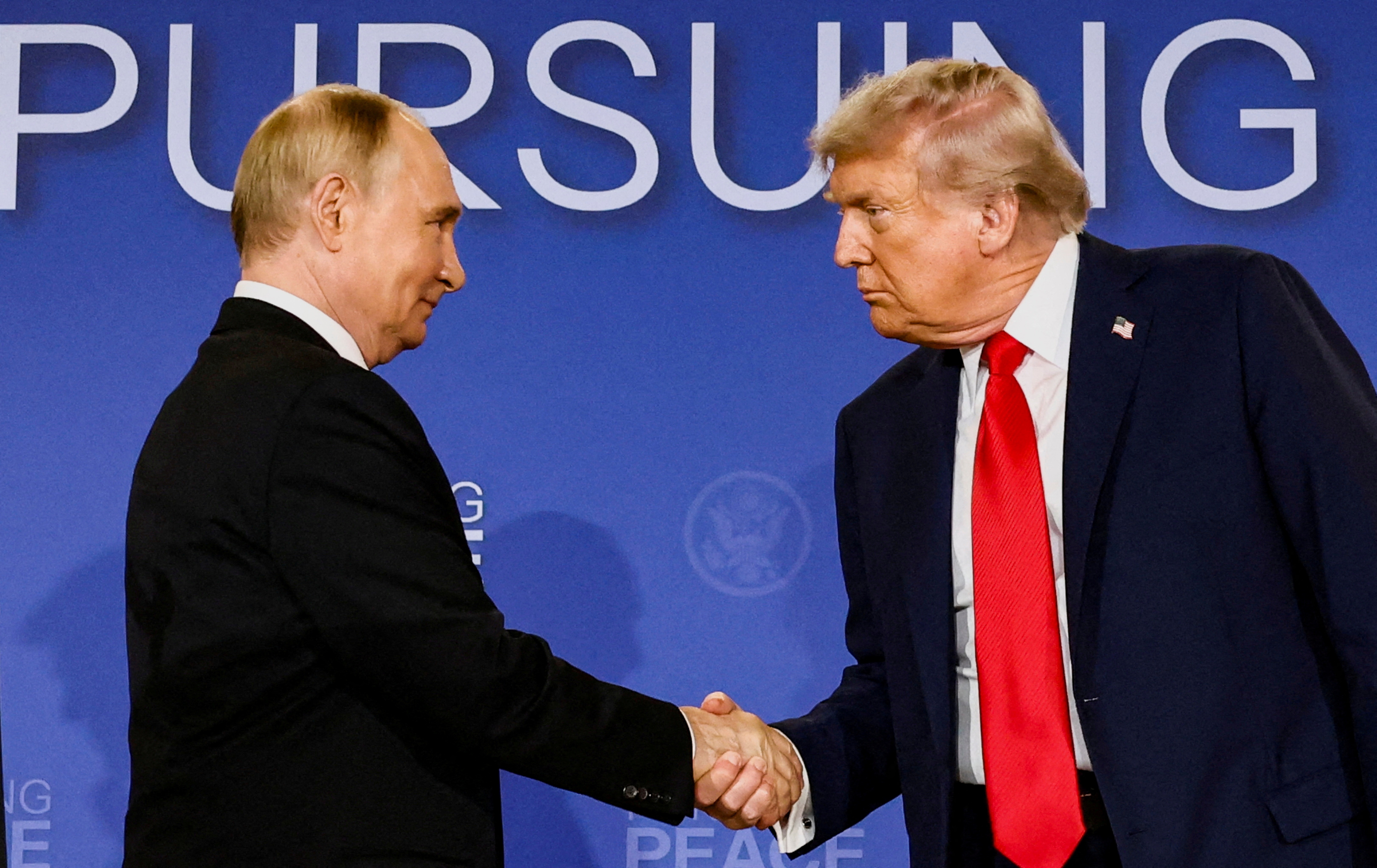 Donald Trump and Vladimir Putin shake hands.